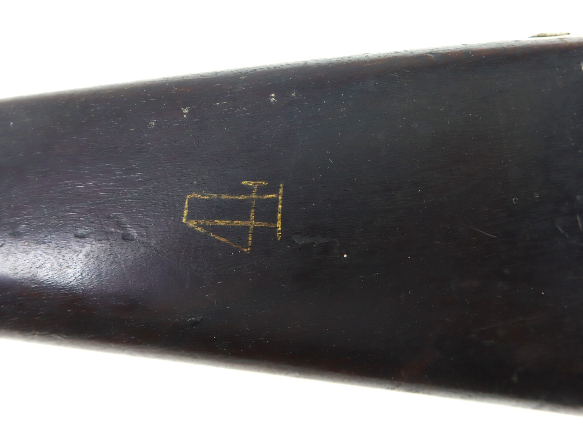 Close-up of a dark wooden rifle stock featuring a simple, yellow arrow and line symbol etched or painted on its surface.