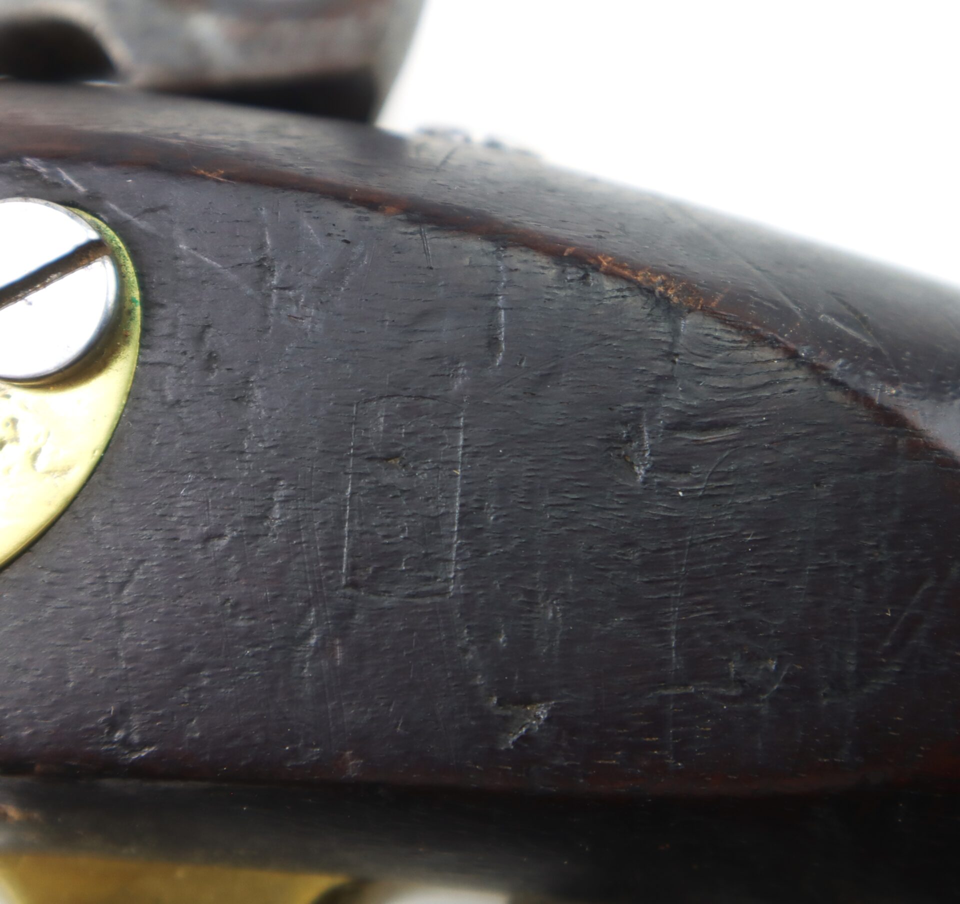 Close-up of a dark wooden object with a brass screw; the surface shows scratches and wear, with part of a metallic component visible at the top.