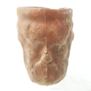 The American Face Pipe, also known as the Grant Presidential Clay Trade Pipe, is a small reddish-brown ancient clay vessel shaped like a human face with worn features and surface cracks, shown against a white background.