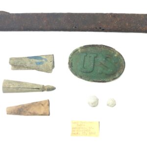 A collection of Civil War relics including a rusty sword scabbard, bullets, a damaged US belt buckle, and a small label with typed text.