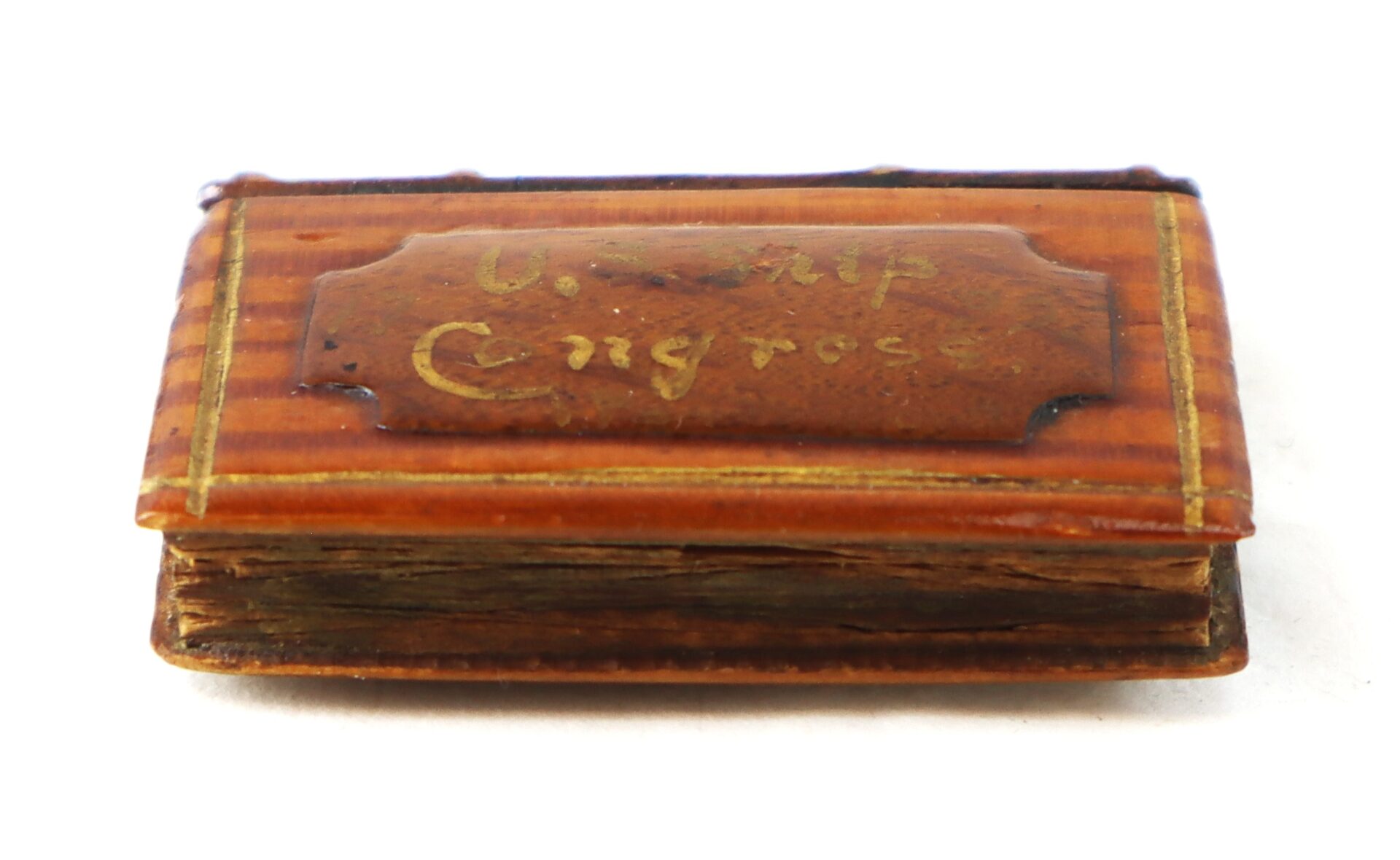 A small, worn, rectangular wooden object resembling a book, labeled "U.S. and Congress" on the cover in faded yellow lettering.