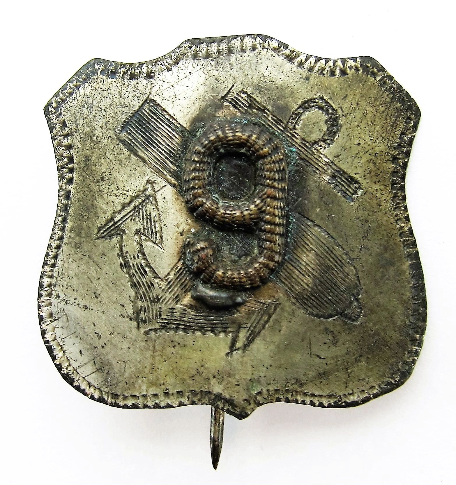 A tarnished 9th Army Corps Badge with a raised number 9 and engraved anchor, cannon, and crossed staff in the background.