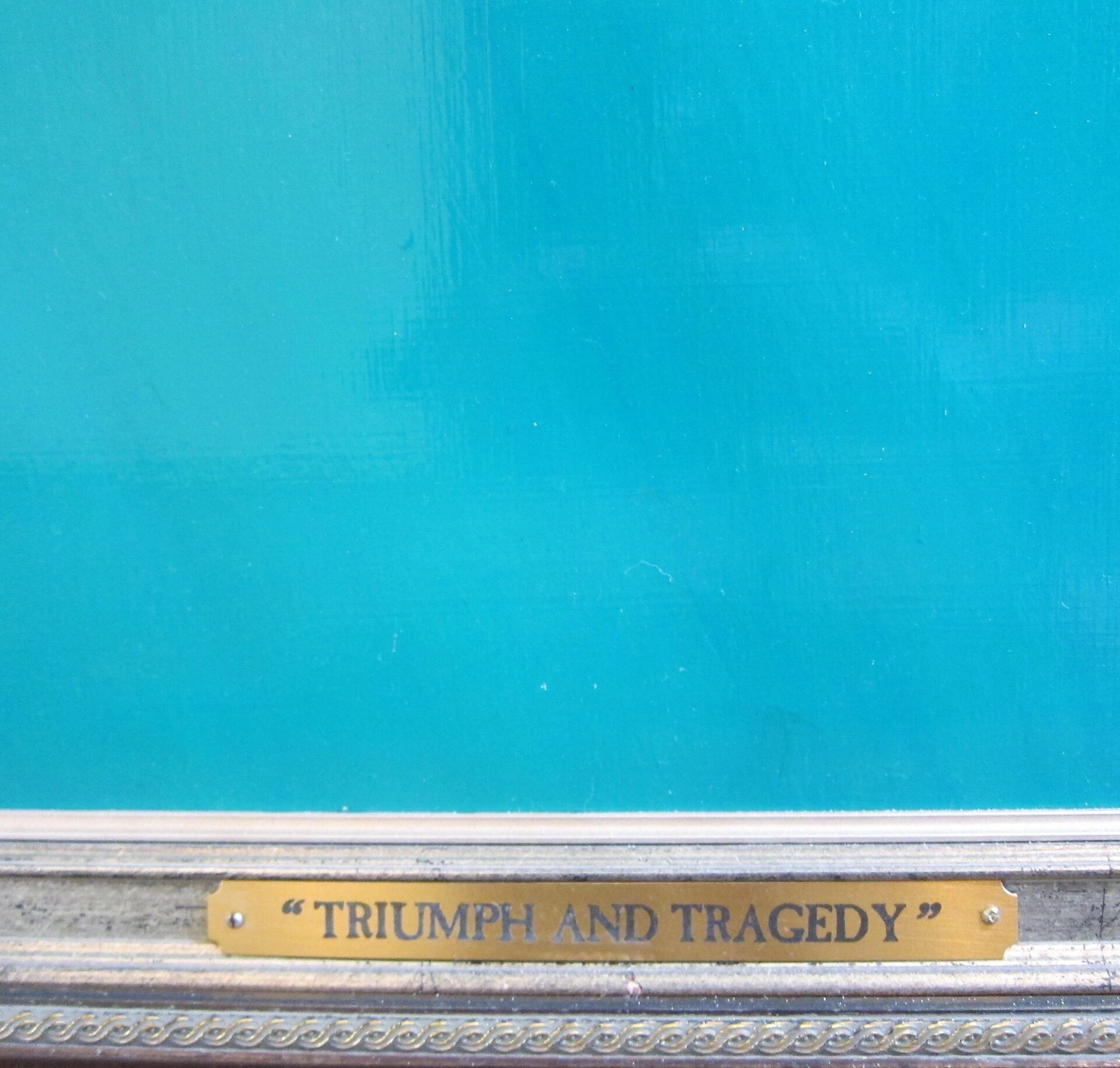 A gold plaque on the framed artwork "Tom Gallo The Sinking of the Hunley" displays its title in black capital letters on a turquoise background.