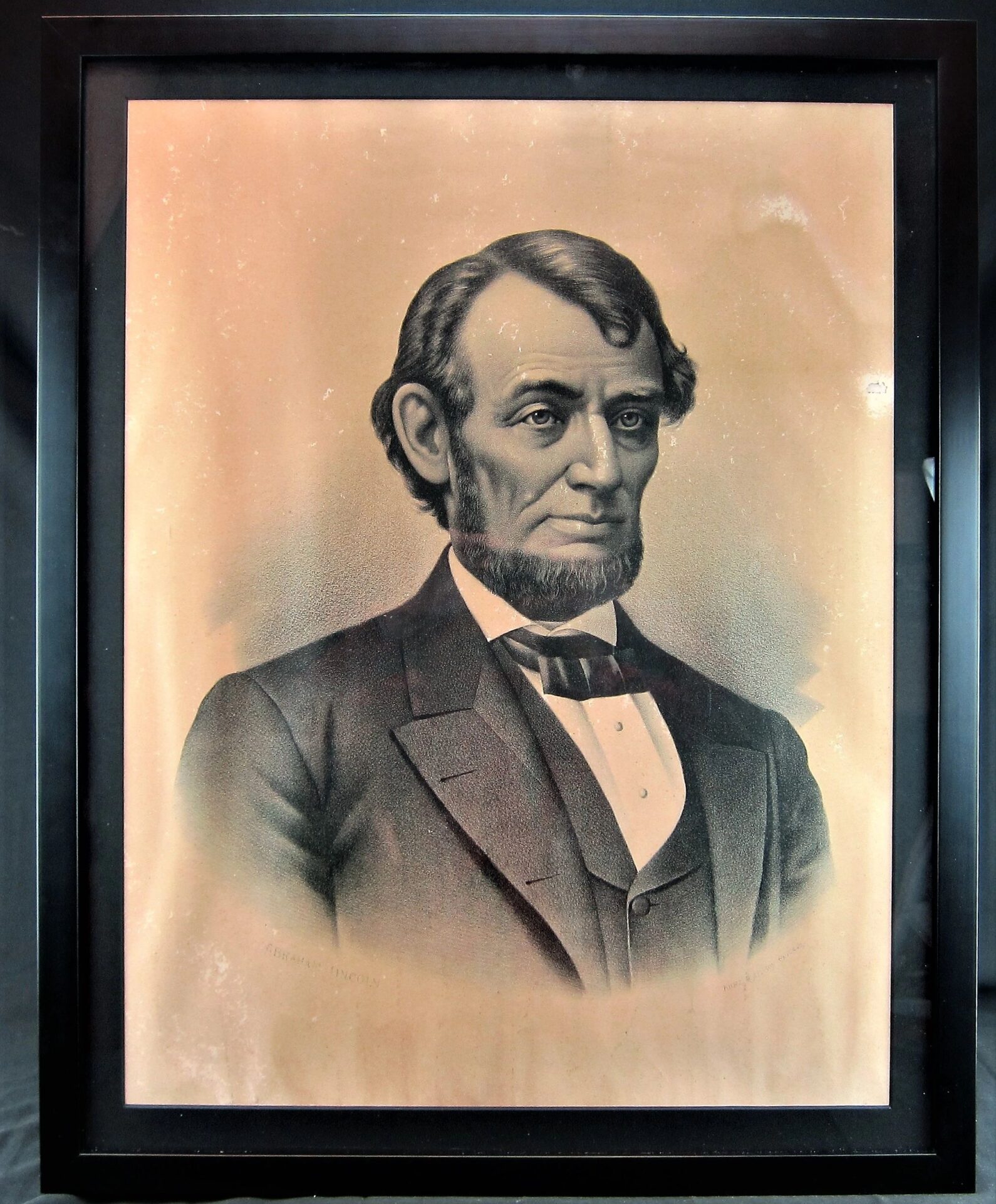 Framed sepia-toned portrait of Abraham Lincoln by Kurtz and Allison, showing him bearded in suit, bow tie, and vest from the chest up against a light background. SOLD.