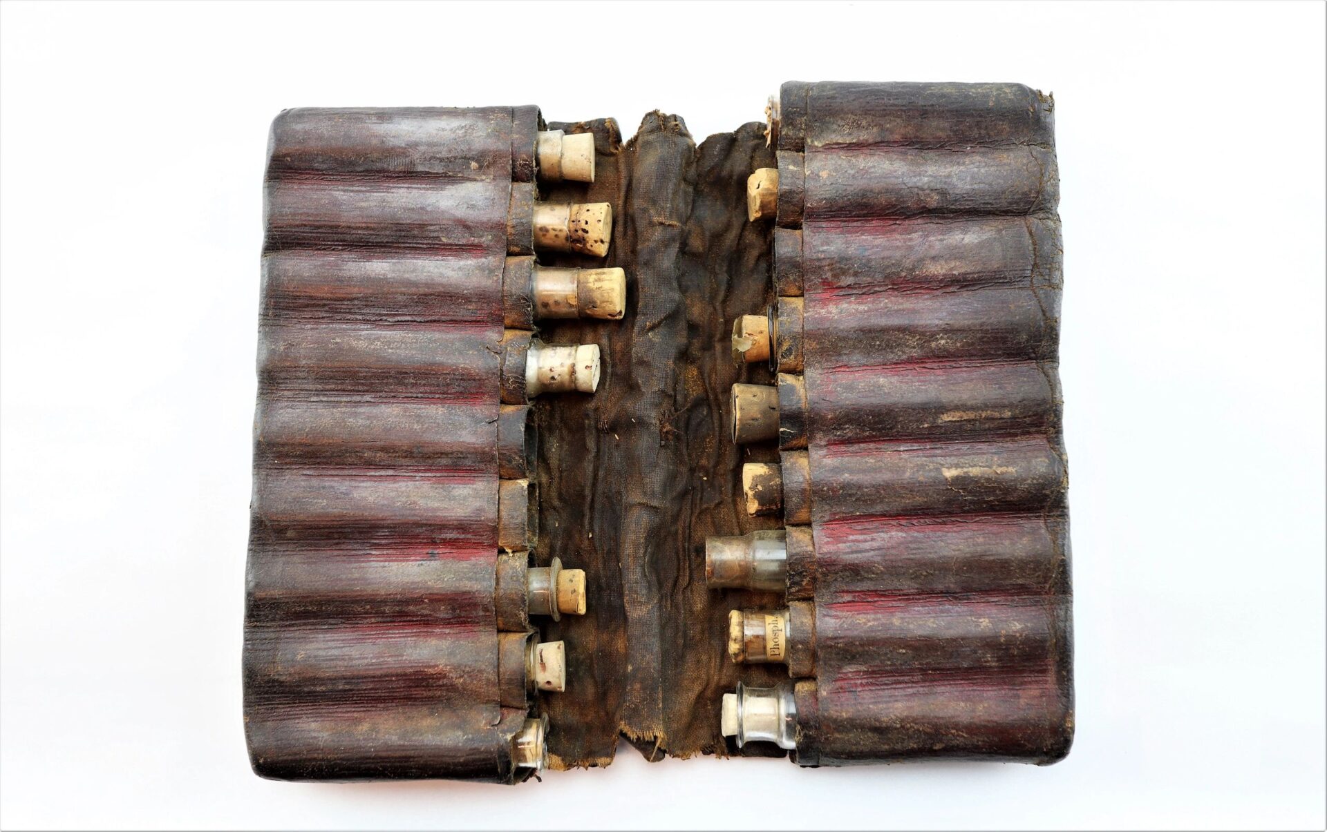 A Leather Apothecary Kit, now sold, features an antique case with cylindrical compartments holding small glass vials—some labeled—displayed open on a white background.