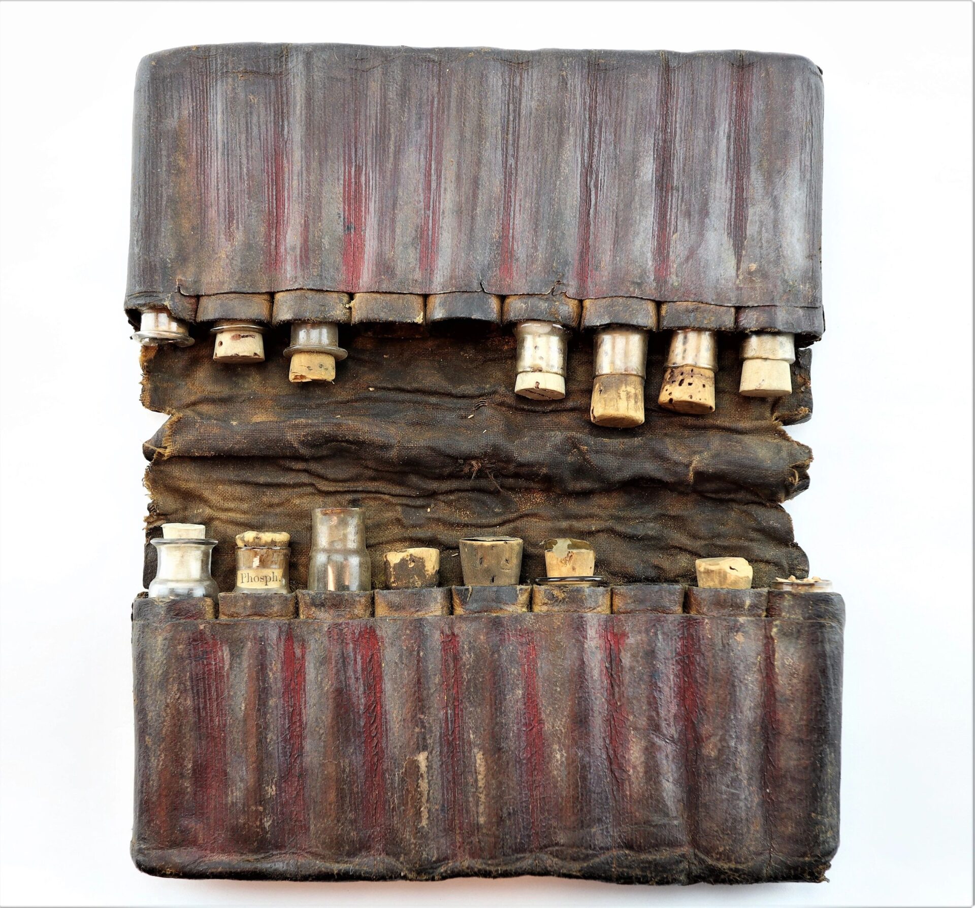 A Leather Apothecary Kit (Sold), featuring two rows of small, cork-stoppered glass vials—some labeled—displayed in a worn leather case against a white background.