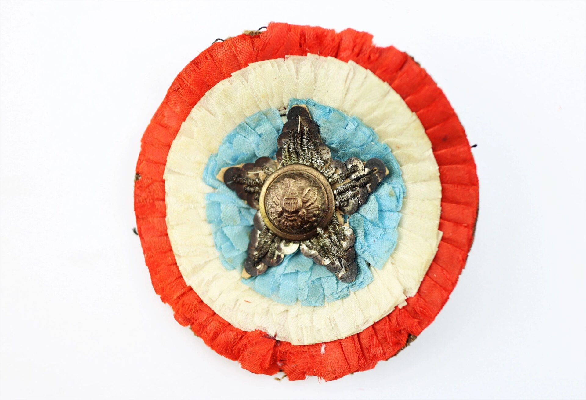 The Patriotic Cockade is a circular ribbon badge with red, white, and blue layers, a metallic star, and a central emblem. / SOLD.