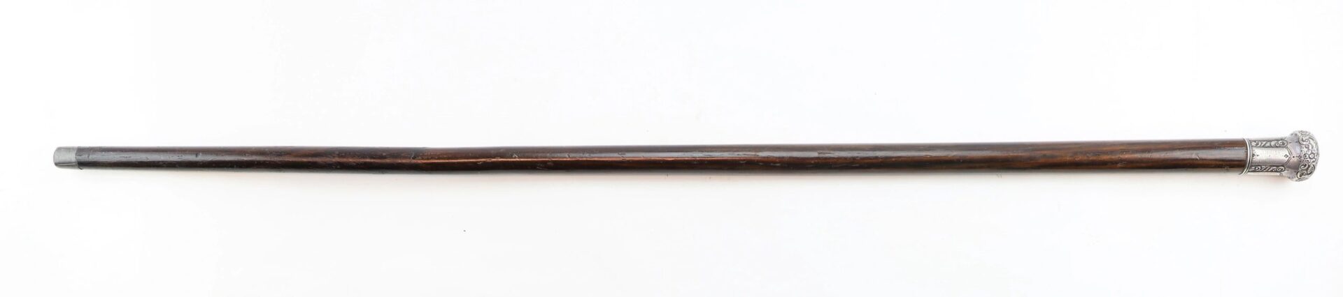 A dark wooden cane made from a Revolutionary War battleship, with a silver-colored ornate handle, displayed horizontally on a white background.