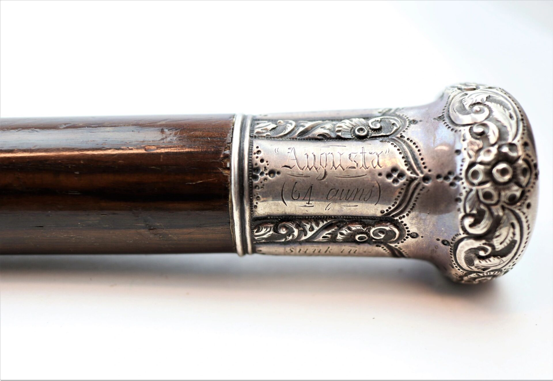 Close-up of a cane made from Revolutionary War battleship wood, featuring an ornate silver handle engraved with "Augusta" and "64 anni.