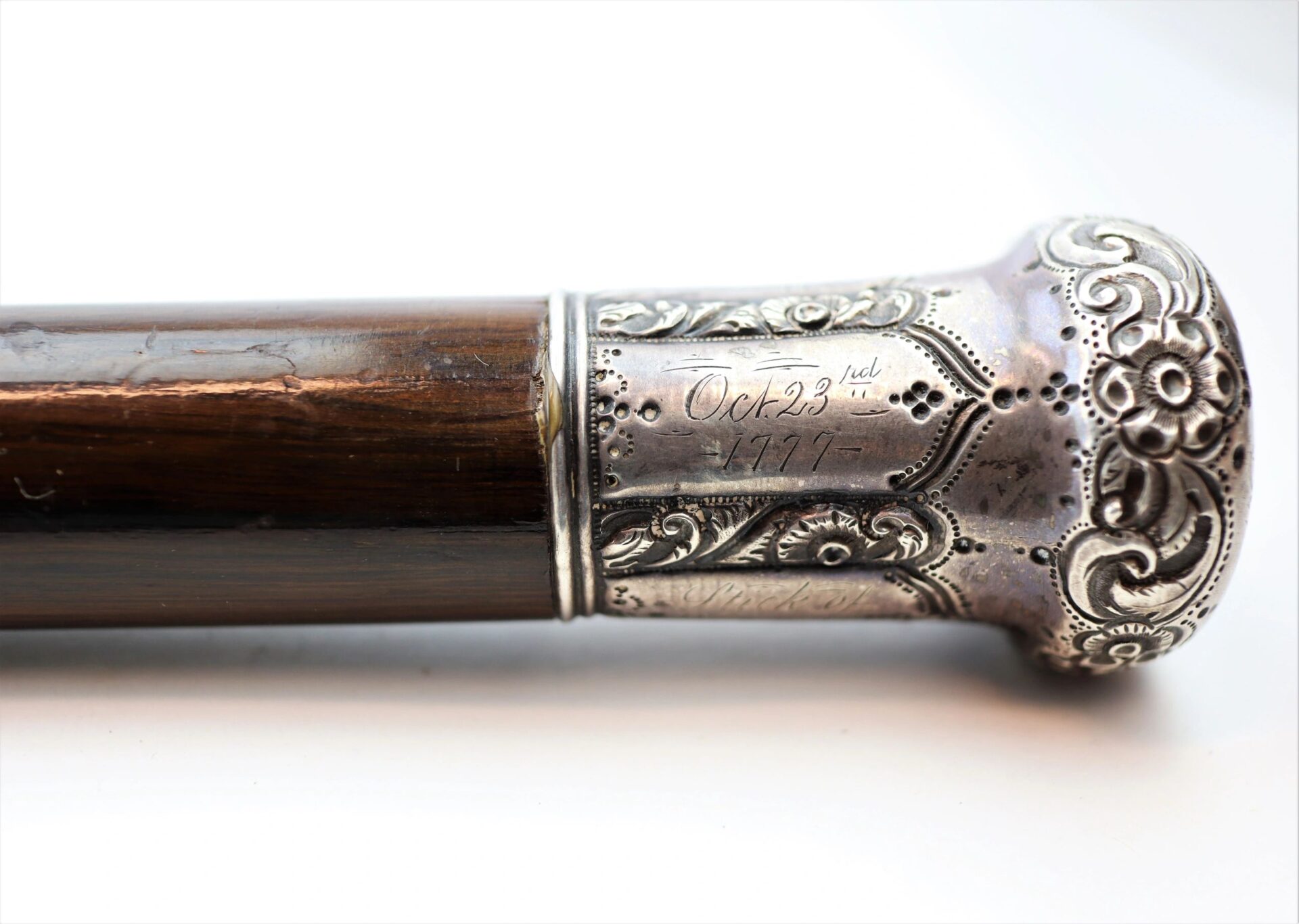 Close-up of a walking cane made from Revolutionary War battleship wood, featuring an ornate silver handle engraved with floral patterns and the date "Oct 23rd 1917.