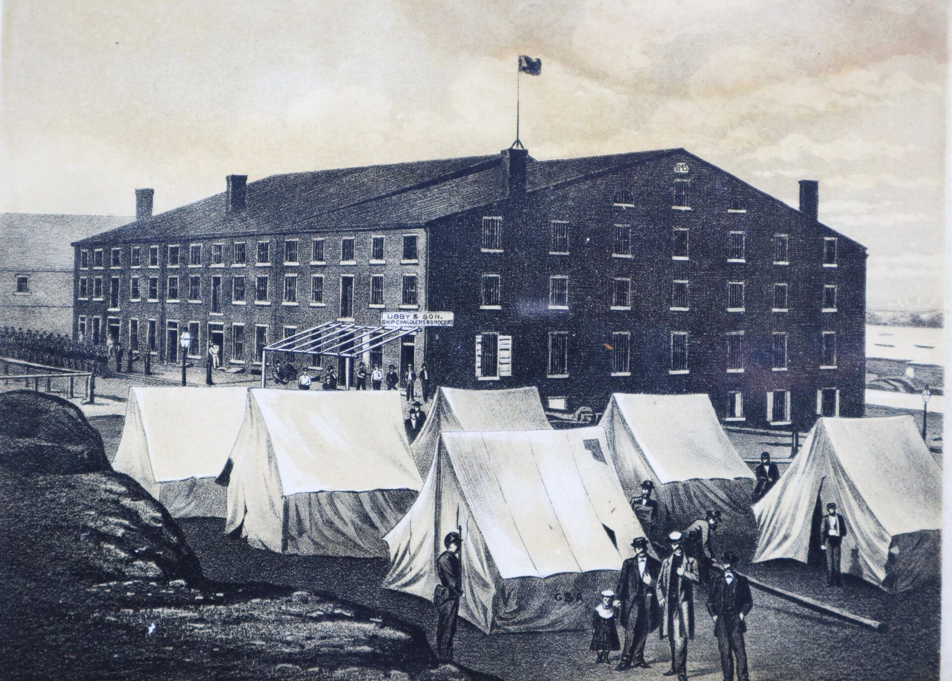 A historical illustration shows several people near large canvas tents in front of Libby Prison, a multi-story brick building with a flag on the roof.