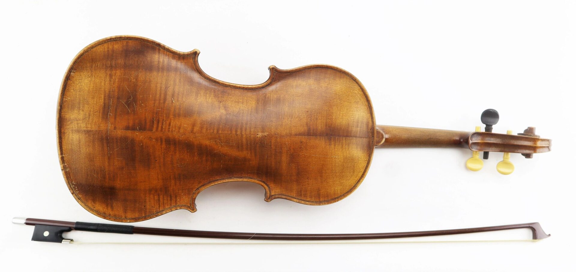A "Violin / Sold" is displayed with its back facing up beside a wooden bow on a white background.