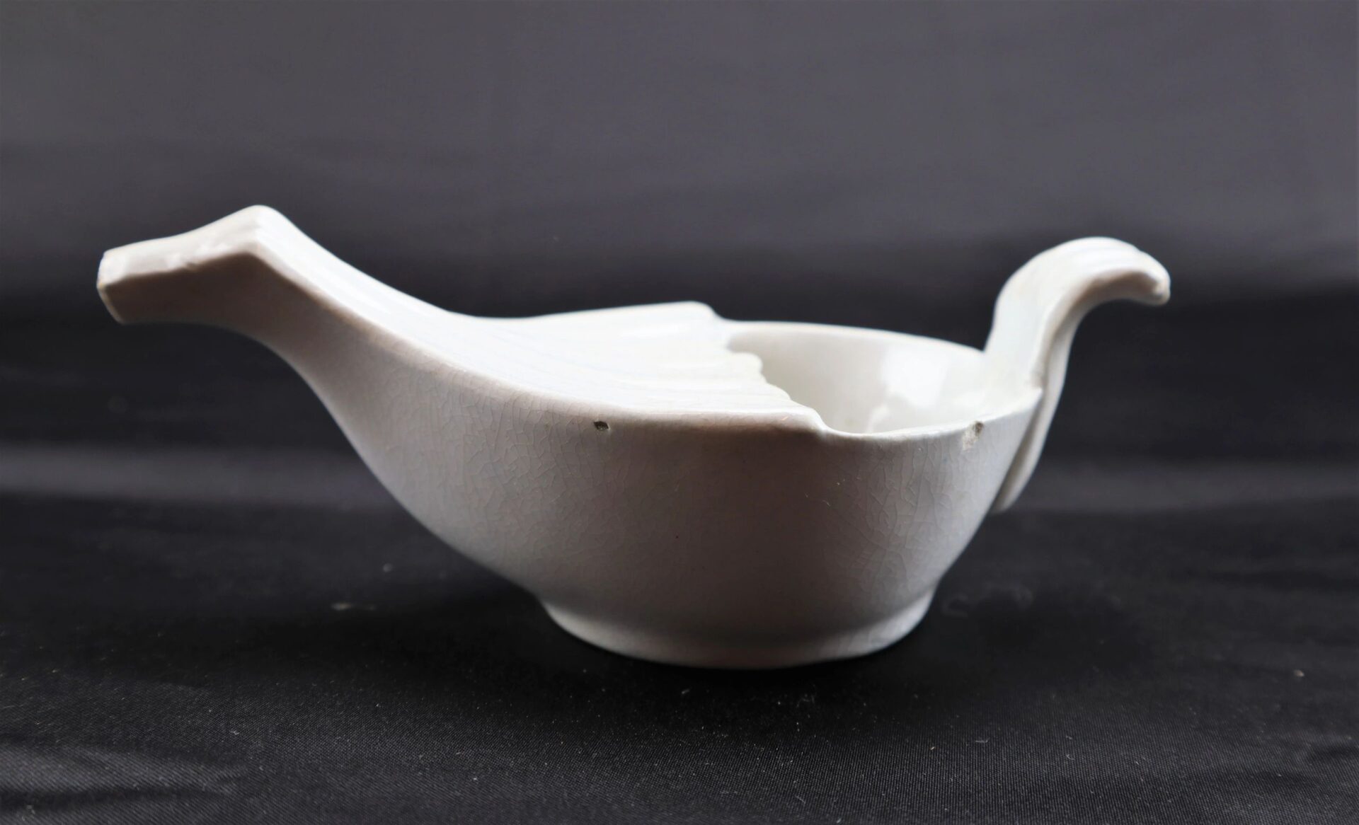 Invalid Feeder, a white ceramic bowl shaped like a bird with a tail-shaped handle and beak-shaped spout, is displayed against a plain black background. Item marked as SOLD.