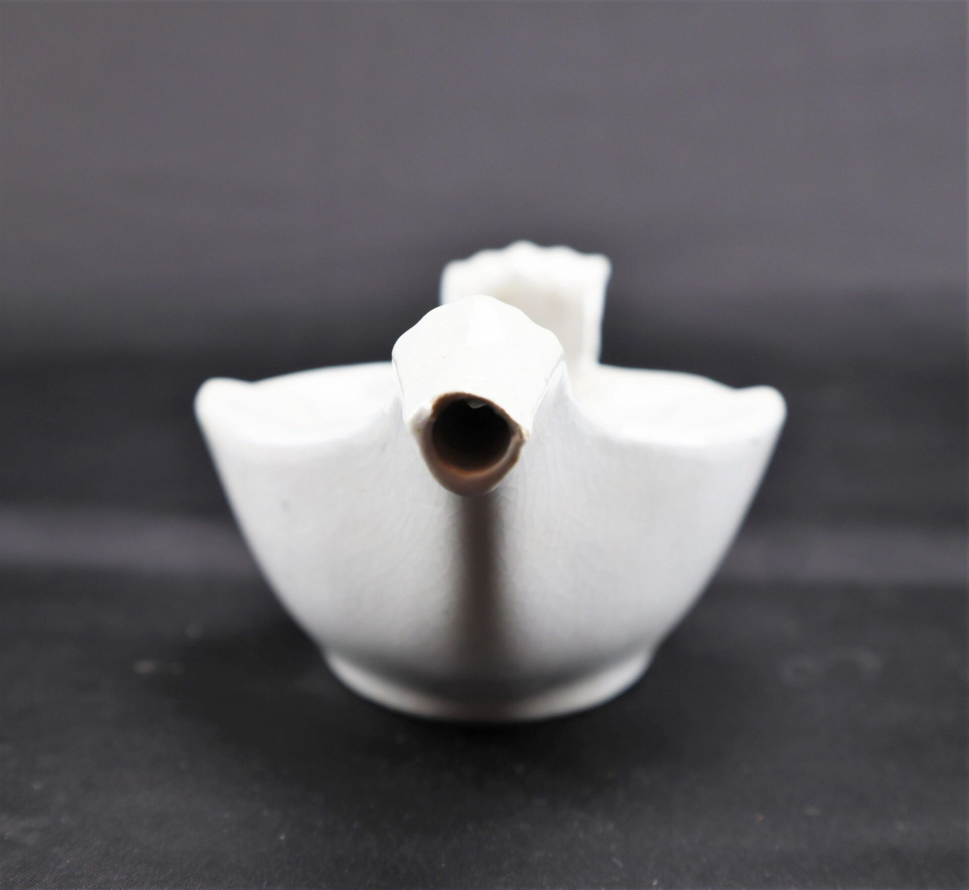 A front-view of the Invalid Feeder, a white ceramic teapot with a wide body and short spout, set against a dark background.