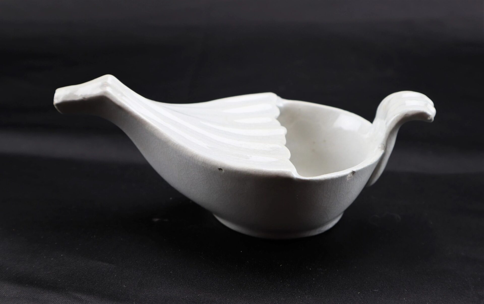 Invalid Feeder (SOLD): A white ceramic bowl shaped like a bird, with its tail and head forming handles, displayed against a black background.