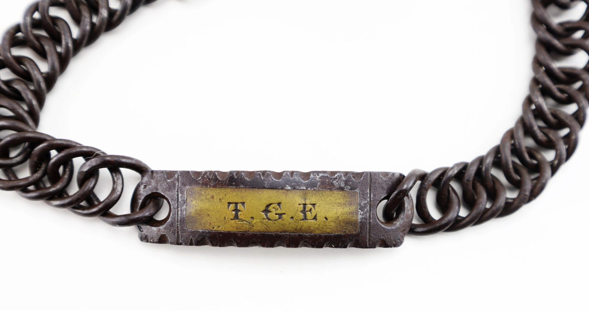 A Civil War Dog / Slave Collar featuring a metal chain bracelet with a rectangular plate engraved "T.G.E." on a yellowed background.