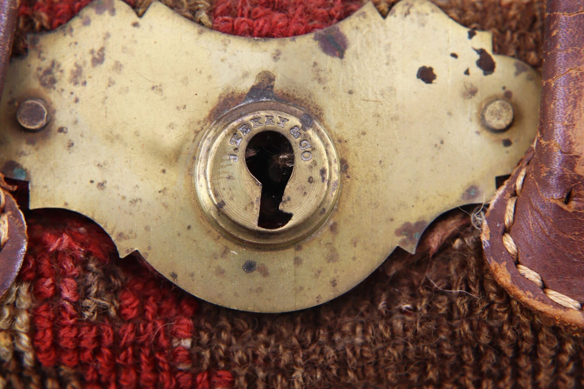 Close-up of a brass lock plate engraved "S. MARTIN & CO" on a Civil War “Carpet Bag,” attached to worn leather and fabric with visible rust and wear. / Sold.