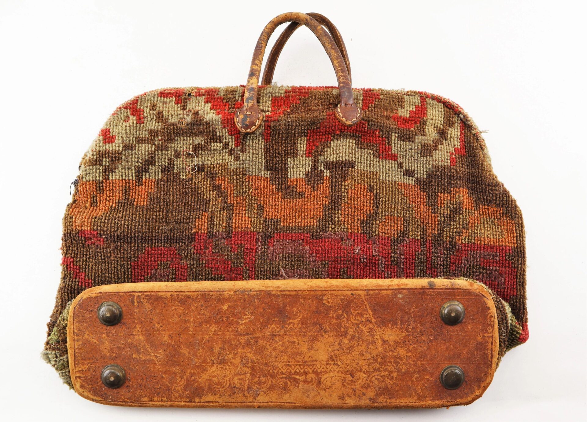 The Civil War “Carpet Bag” features leather handles, a worn leather base, and tapestry-style fabric in red, brown, and beige tones.