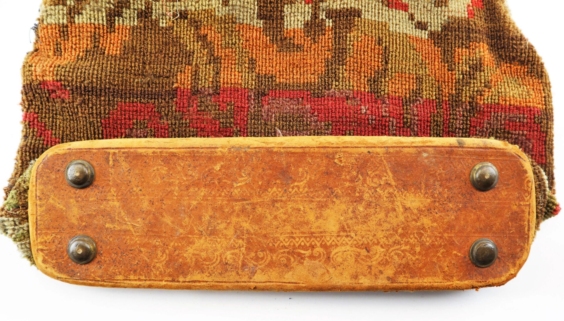 A close-up of the worn leather bottom of the Civil War “Carpet Bag,” showing four metal studs and patterned fabric above.