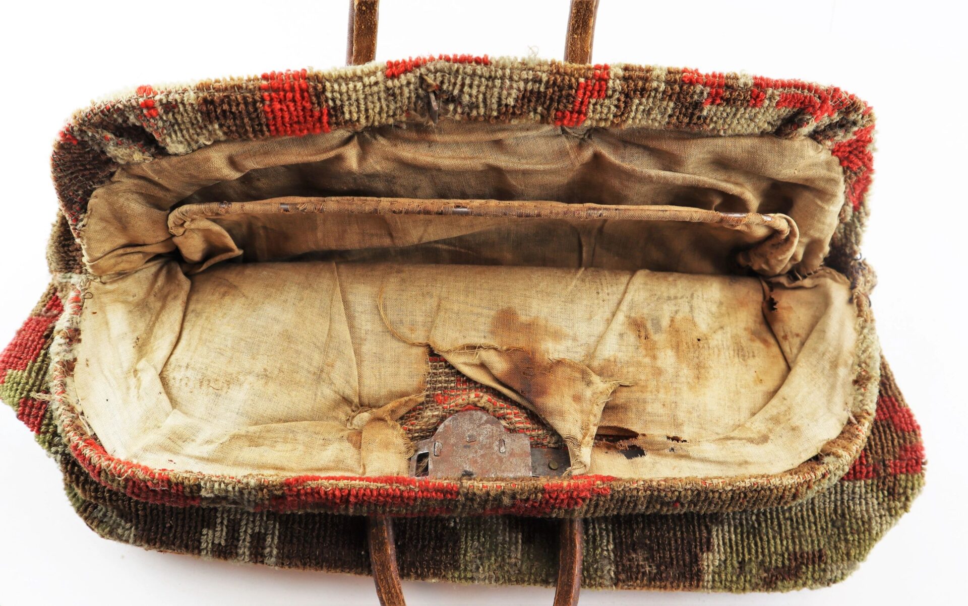An open, old Civil War “Carpet Bag” with a worn fabric exterior, stained and discolored interior, and visible metal clasp.