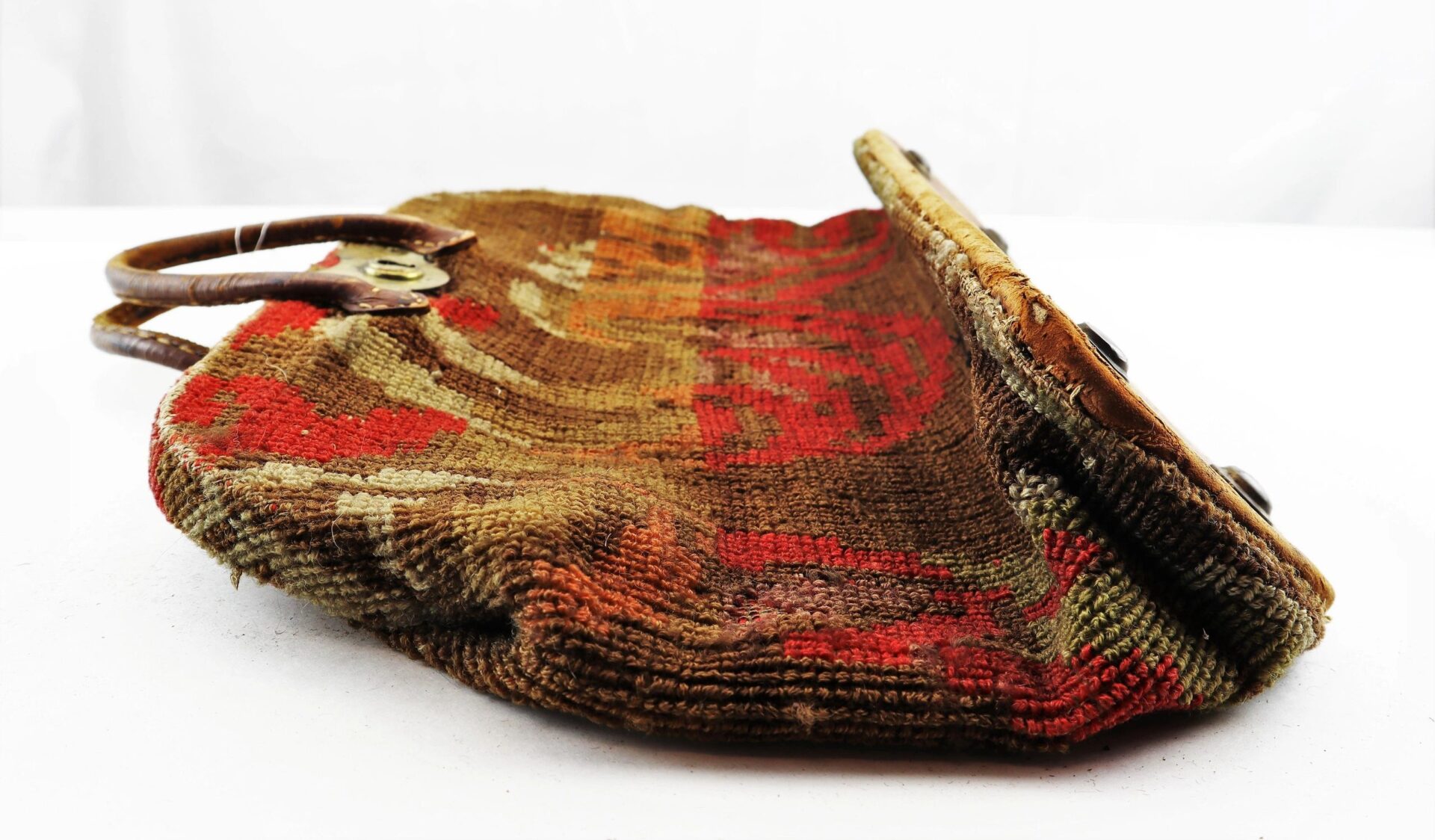 A Civil War “Carpet Bag” with a vintage, multicolored tapestry design, leather handles, and metal clasp is shown lying flat on a white surface. Sold.