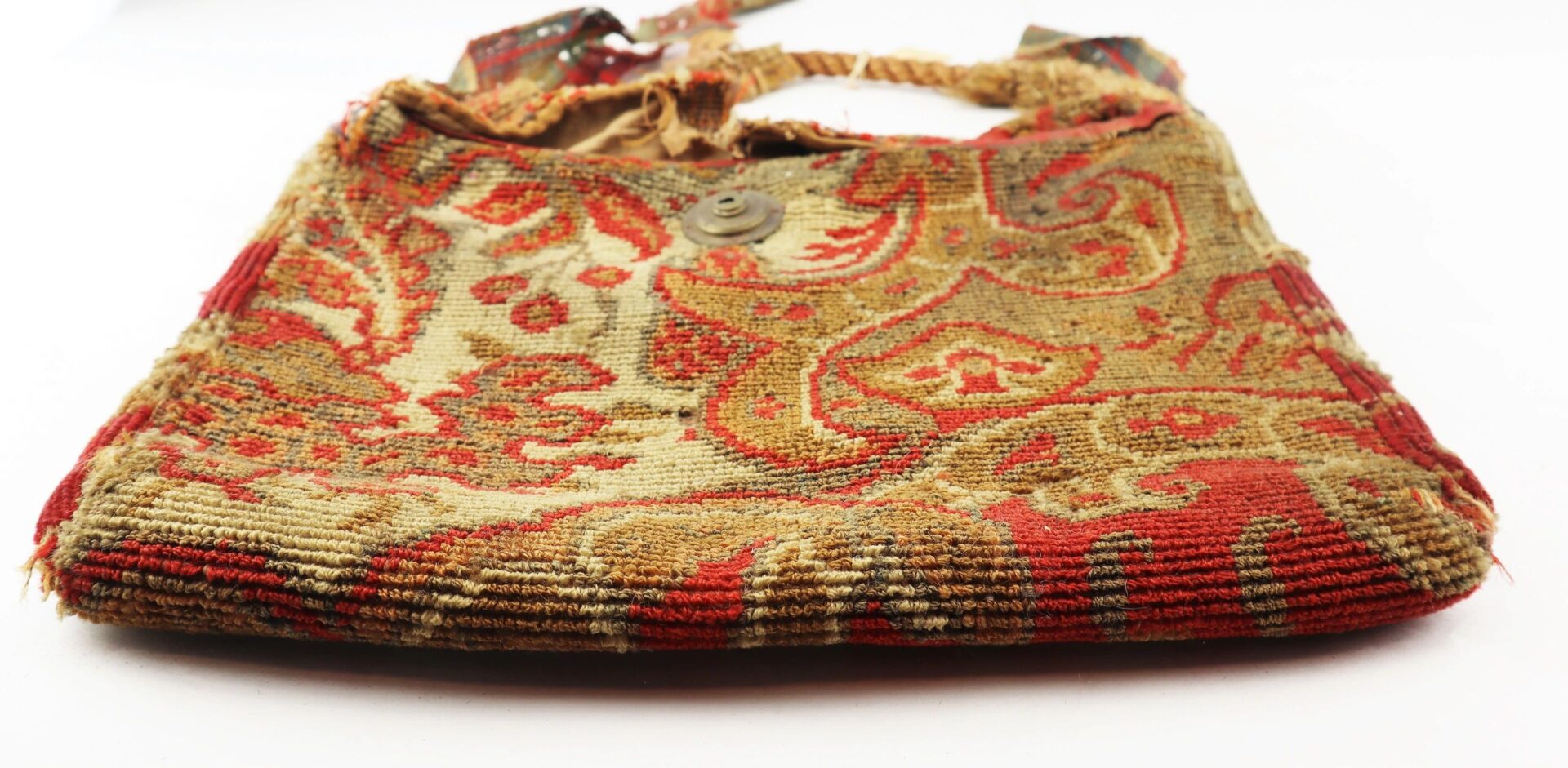 A flat, rectangular Civil War “Carpet Bag” with a worn multicolored paisley pattern, braided strap, and button closure is displayed on a white background. / SOLD.