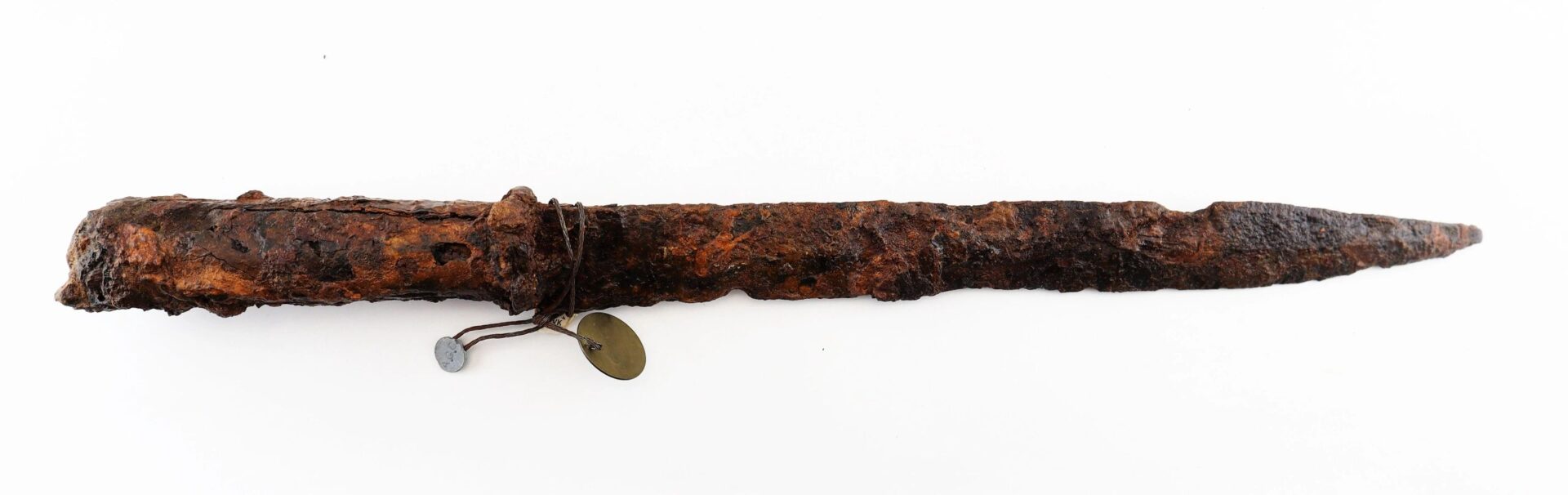 A Confederate “Bridle-Cutter” Pike with a rusted, ancient metal blade and handle, attached to two identification tags by string, is shown against a white background.