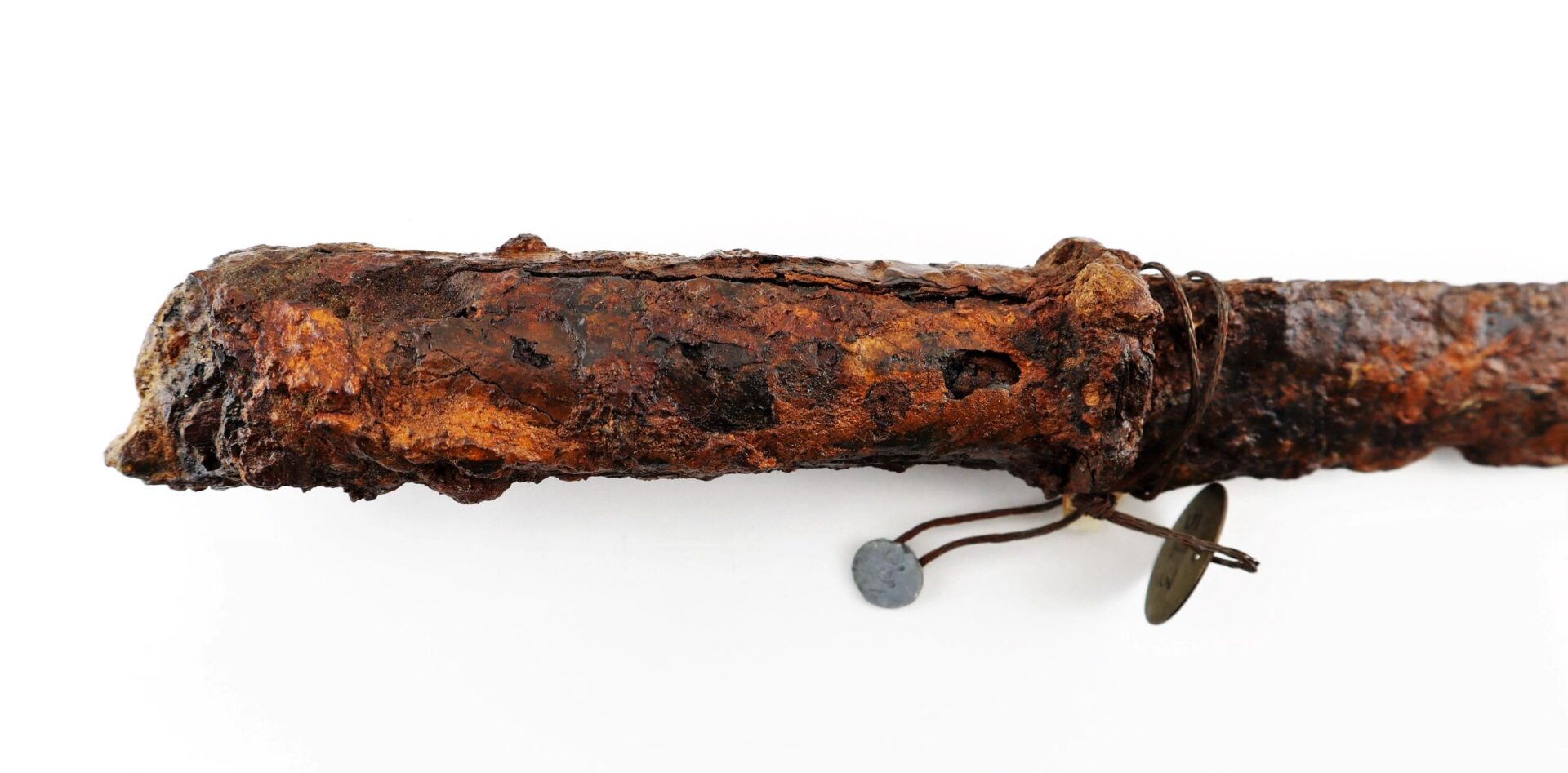A Confederate “Bridle-Cutter” Pike, heavily rusted and cylindrical with attached wire and small round metal tags, displayed on a white background.