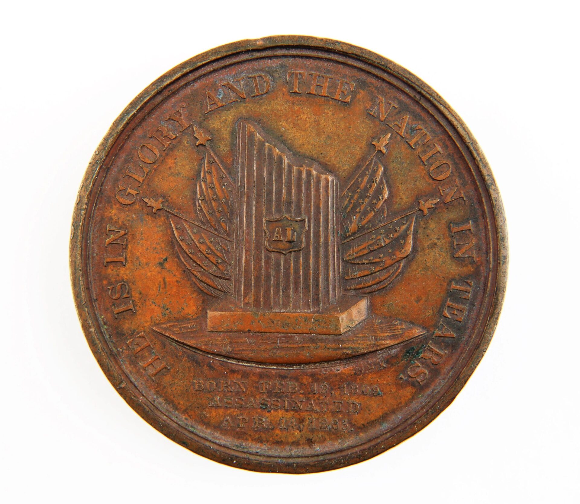 A worn Lincoln 1865 Assassination Medal depicting a monument with flags, inscribed "HE IS IN GLORY AND THE NATION IN TEARS," commemorating Lincoln’s assassination.
