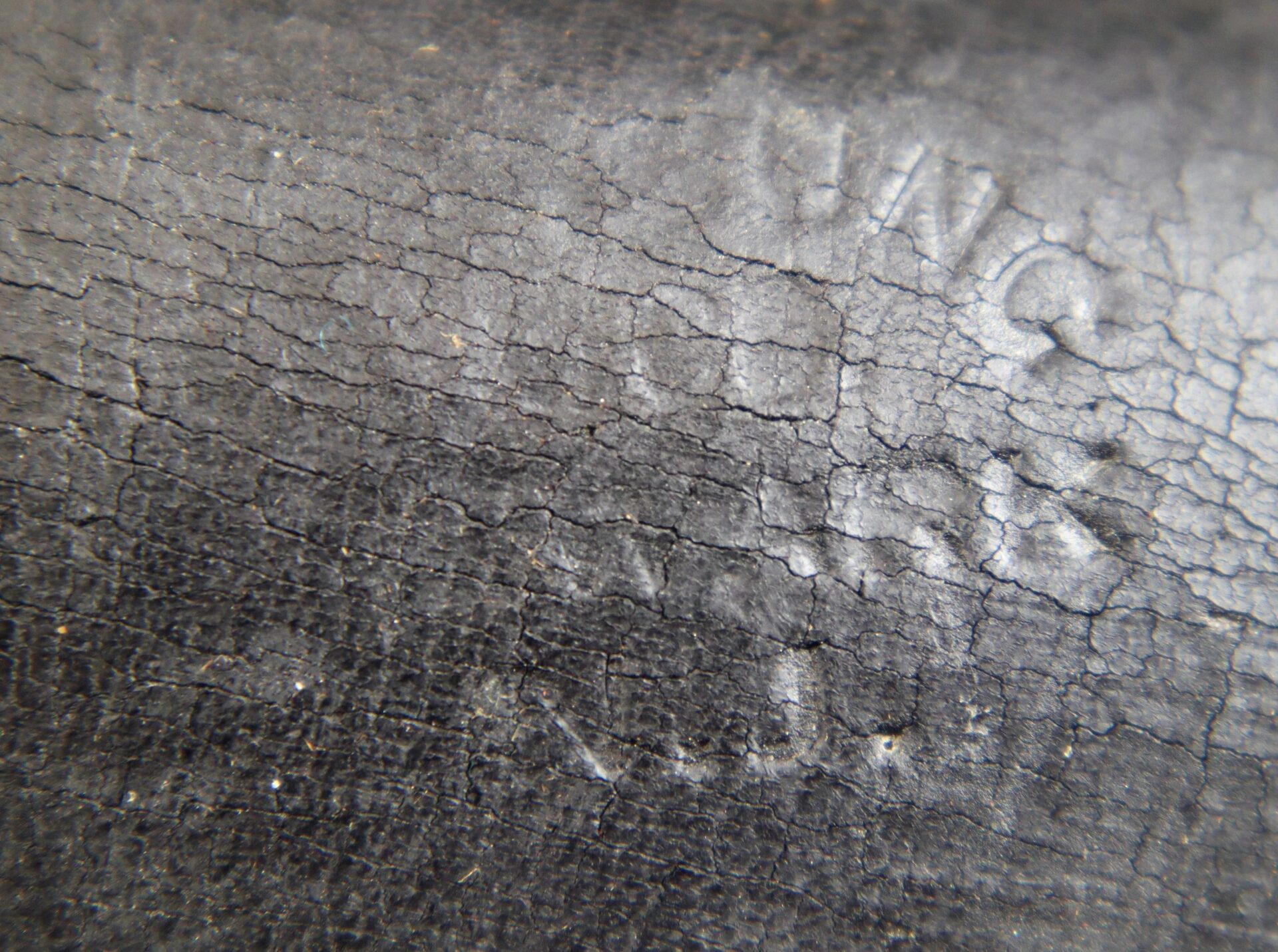 Close-up of cracked, weathered black rubber surface on Civil War Percussion Cap Box with faint, partially visible embossed text.