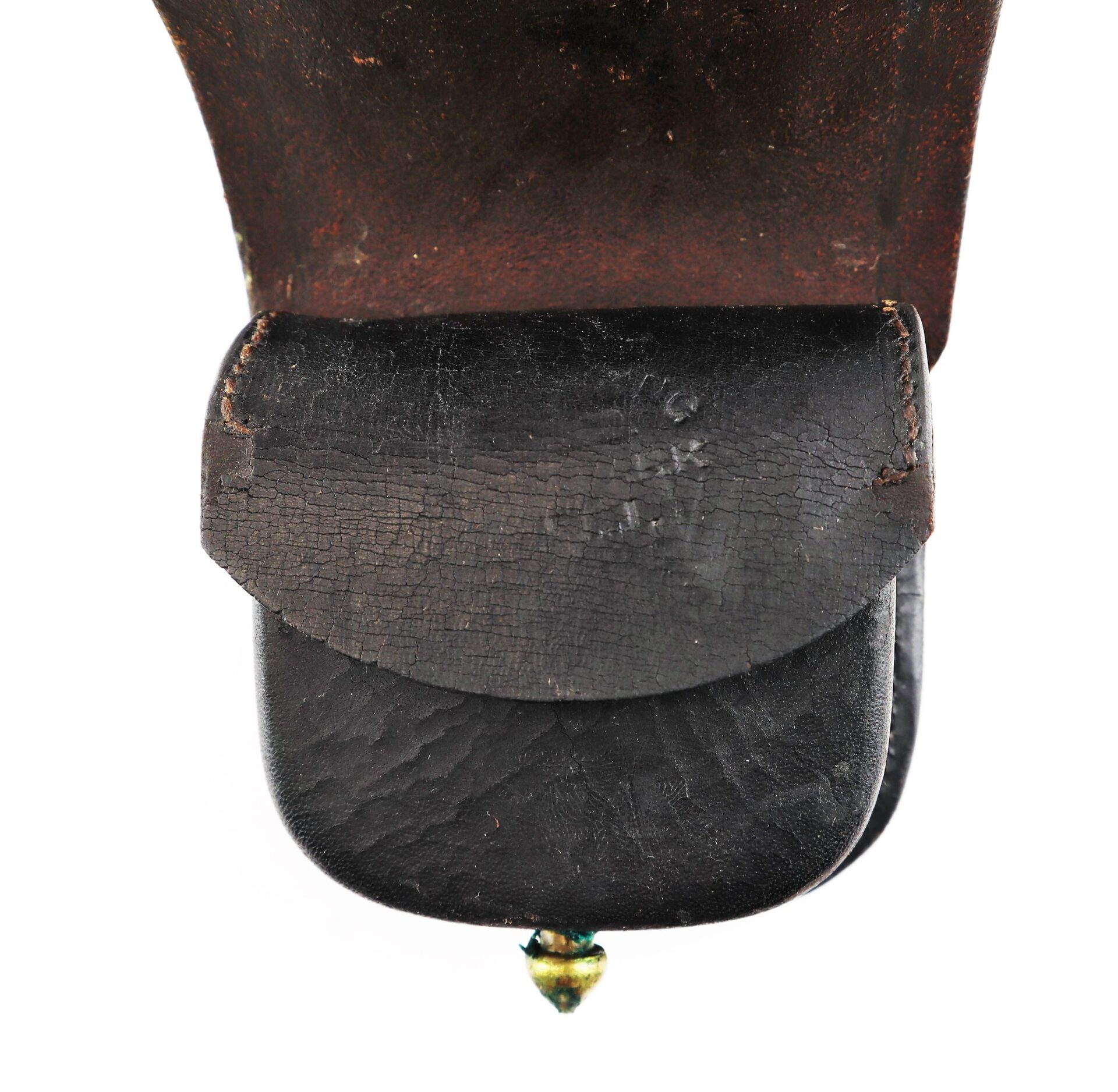 Close-up of a worn Civil War Percussion Cap Box, black leather with a small brass button at the bottom, attached to a brown leather surface.
