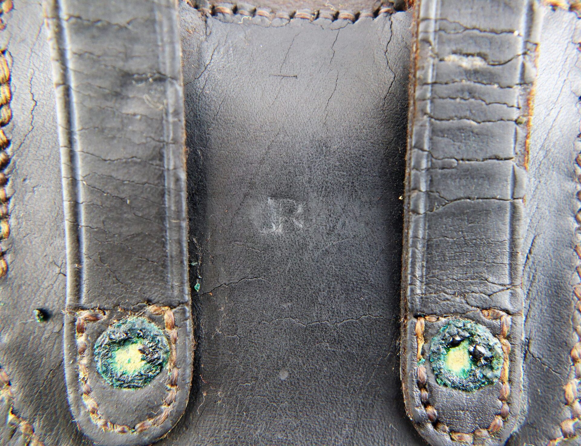 Close-up of worn black leather Civil War Percussion Cap Box with two stitched straps, green corrosion on metal rivets, and faint "ARM" lettering in the center. / SOLD.