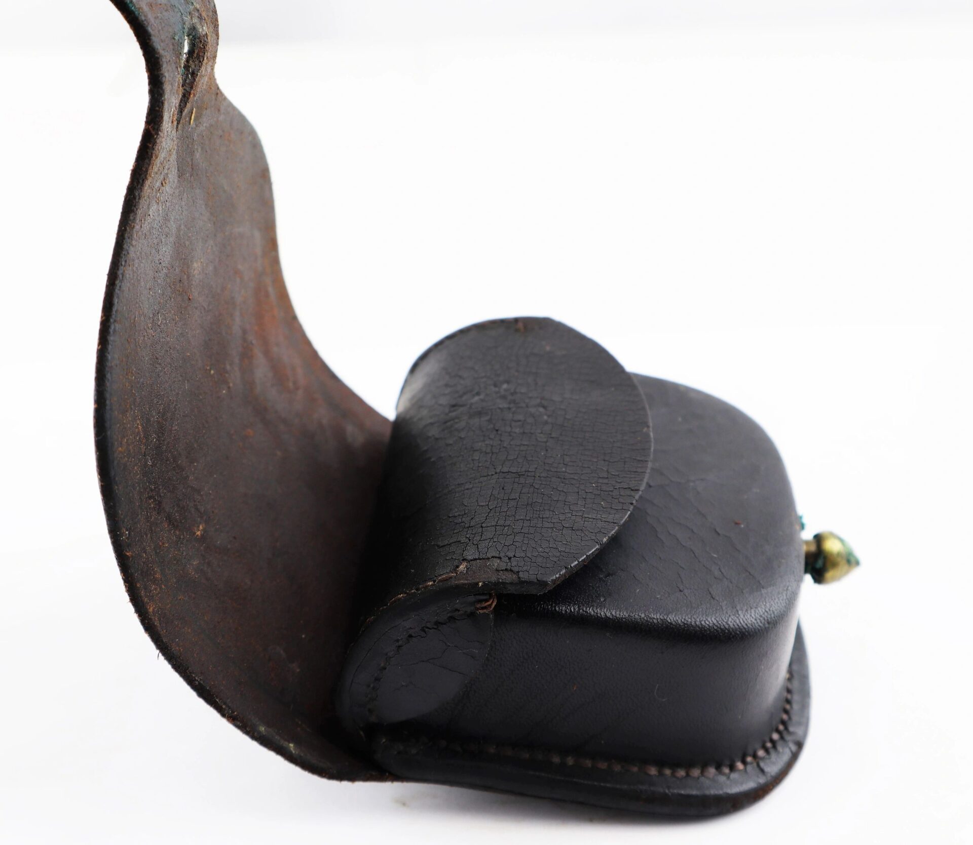 A Civil War Percussion Cap Box / SOLD—worn black leather with a partially open flap on a curved, rusted metal plate.
