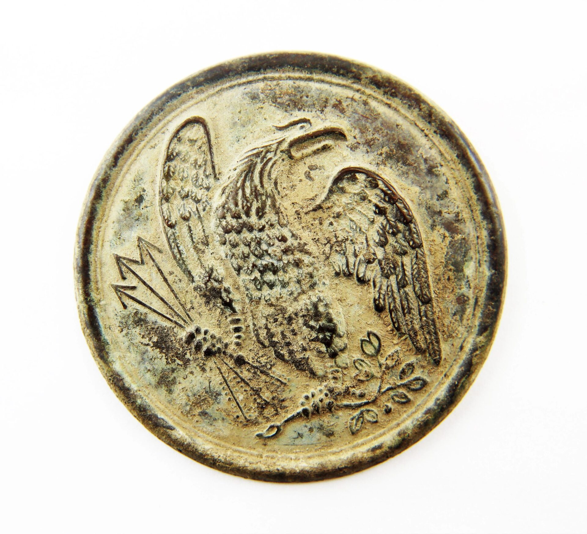 An excavated U.S. Eagle Breast Plate, round and weathered, features an engraved eagle with outstretched wings clutching arrows and an olive branch.