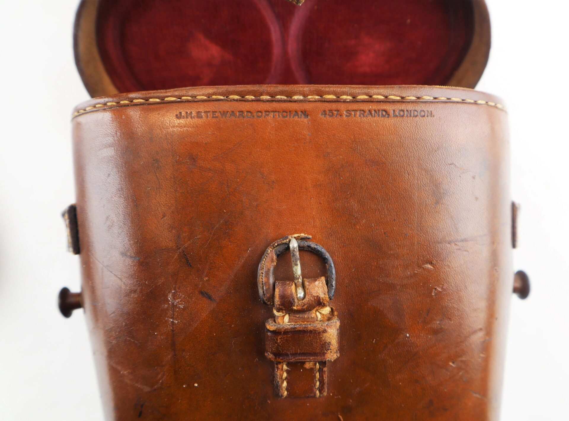 Close-up of Civil War Field Glasses and Case / SOLD: brown leather case with a metal buckle, embossed "J.McTEWARD OPTICIAN 457, STRAND, LONDON," and partially visible red interior lining at the top.