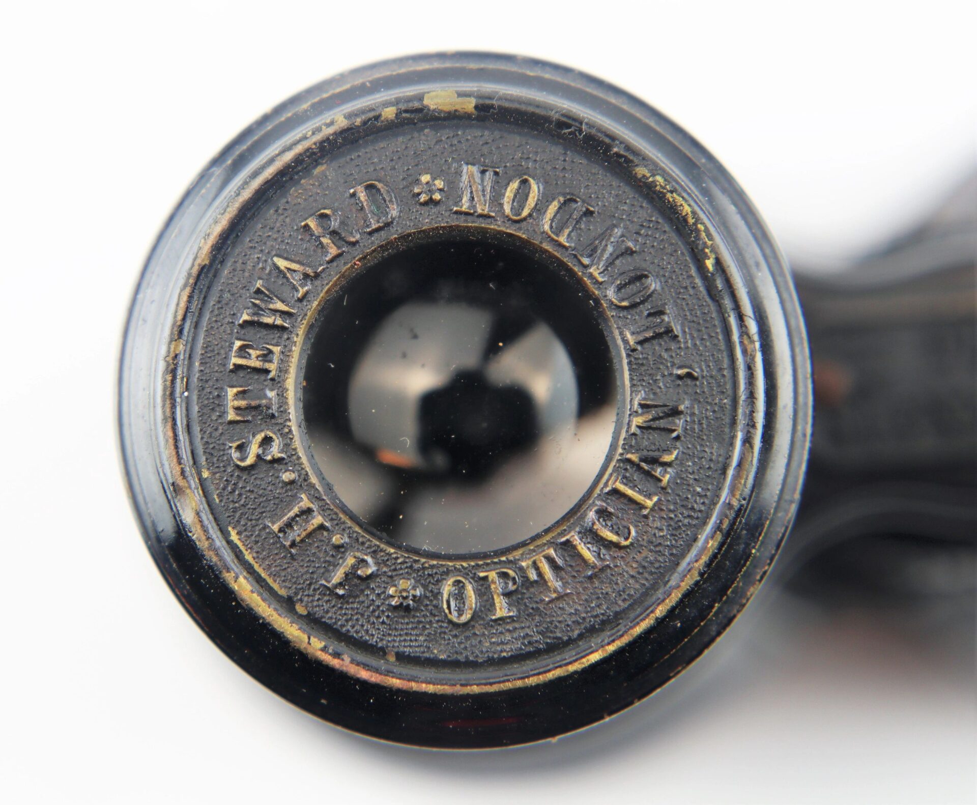 Close-up of Civil War Field Glasses and Case, featuring a vintage black optical part engraved with "J.H. Steward, Optician, London" around the lens.
