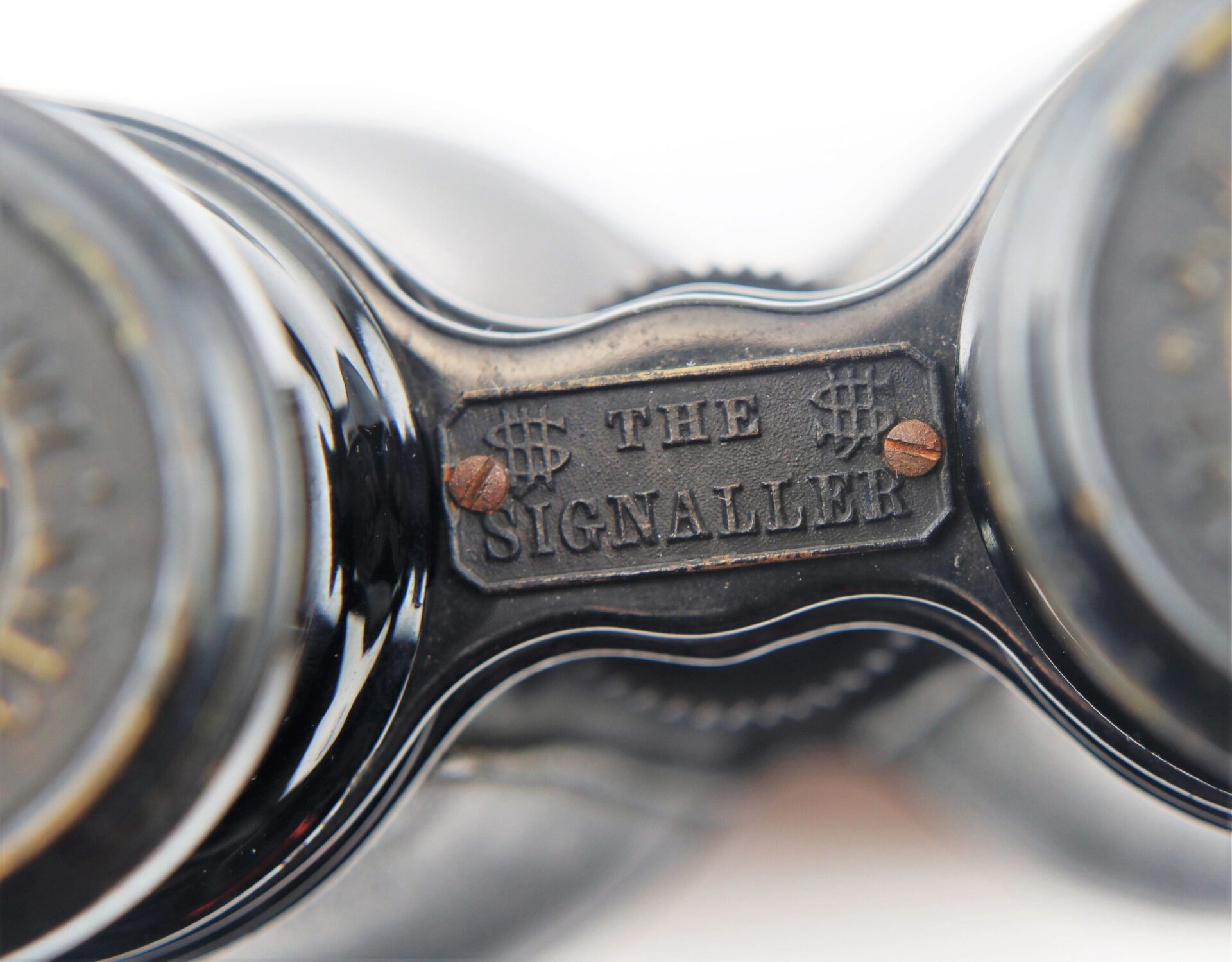 Close-up of a metal plate on the Civil War Field Glasses and Case, labeled "THE SIGNALLER," with two screws and dollar signs on either side of the text.