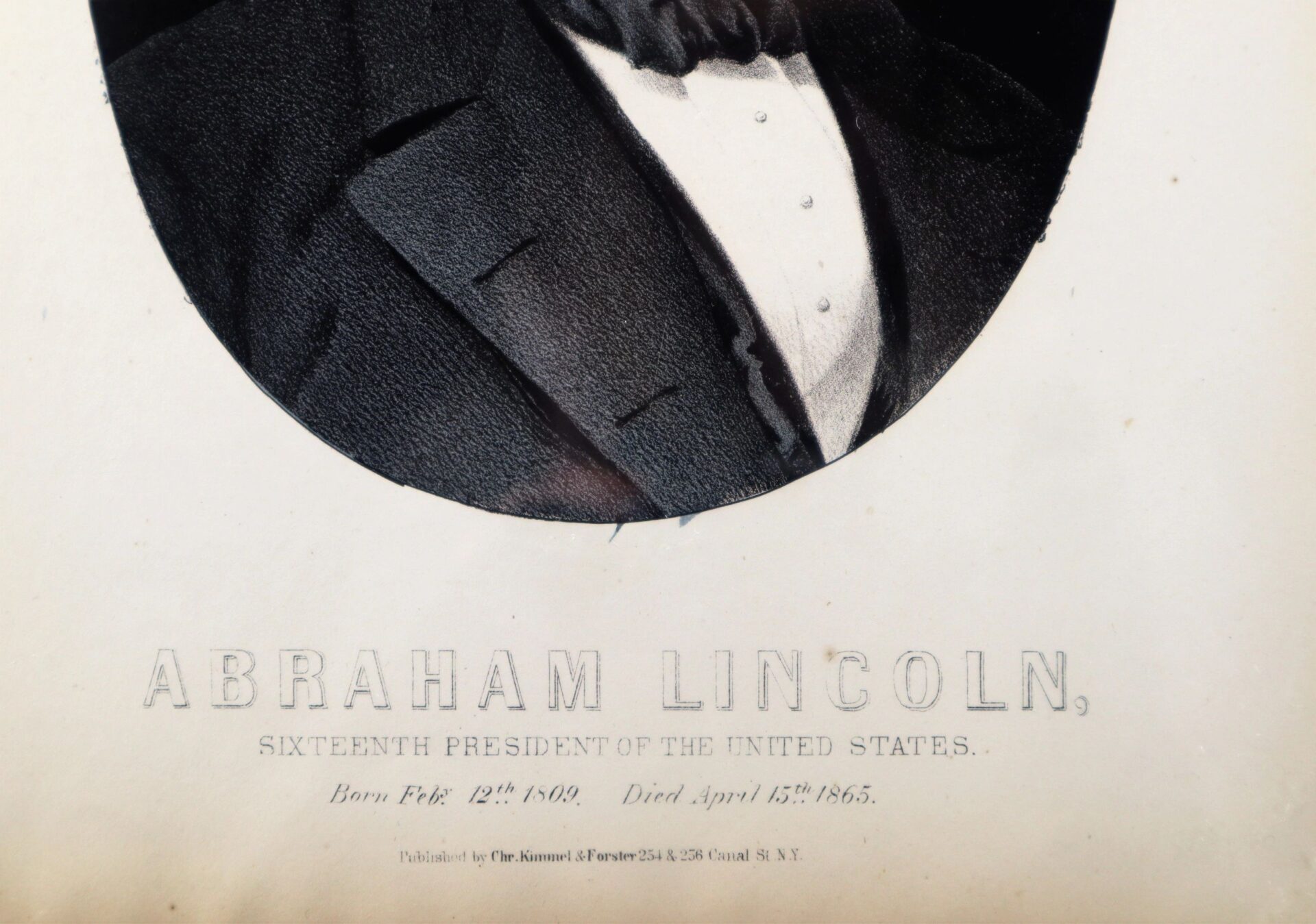 Partial image of the Abraham Lincoln Lithograph, depicting the torso and bowtie of Abraham Lincoln. Text: "Sixteenth President of the United States. Born Feb. 12, 1809. Died April 15, 1865.
