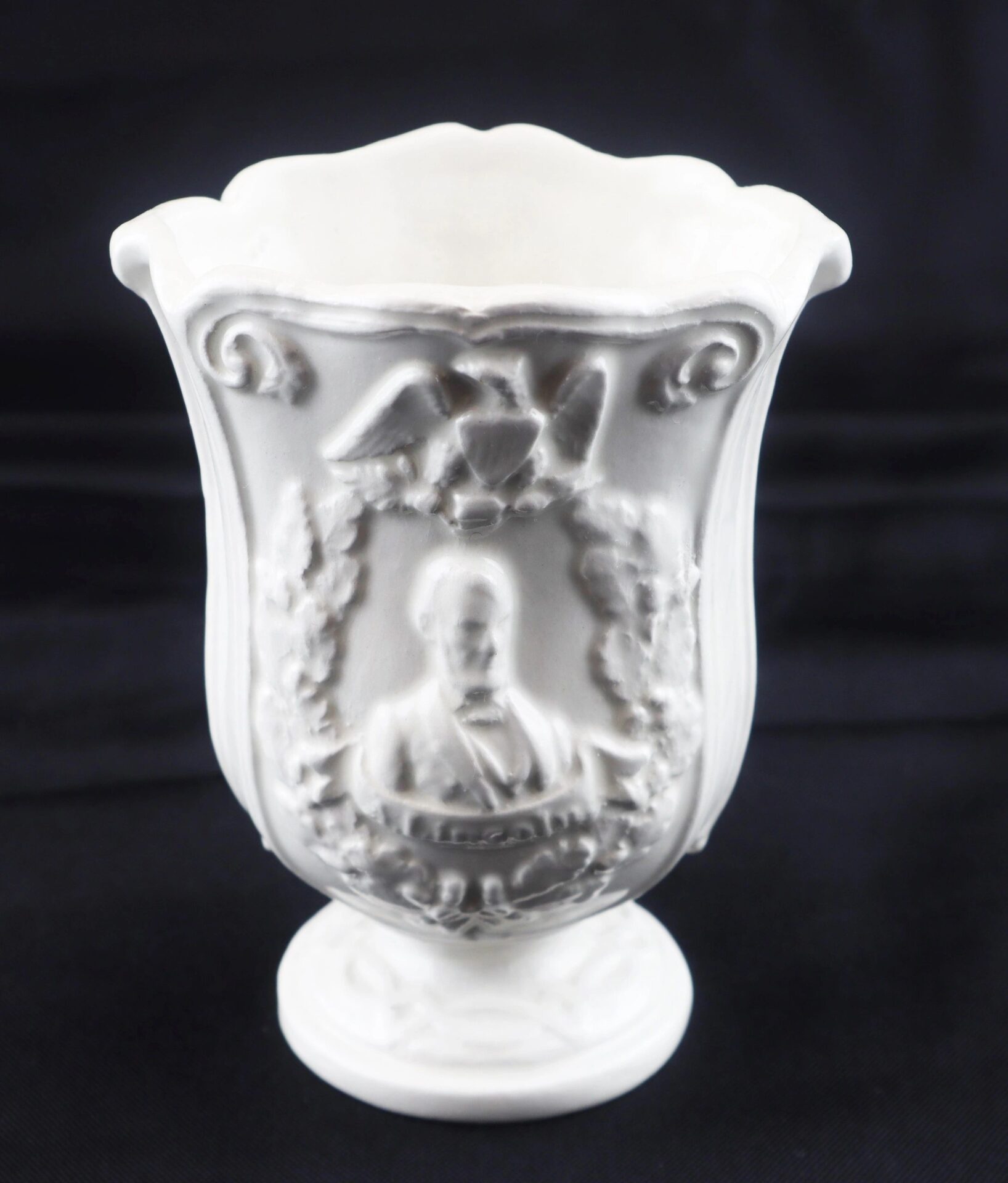The Civil War Vintage Abraham Lincoln Stoneware Vase features an embossed portrait of Abraham Lincoln framed by a laurel wreath and topped with an eagle, all set against a plain dark background.