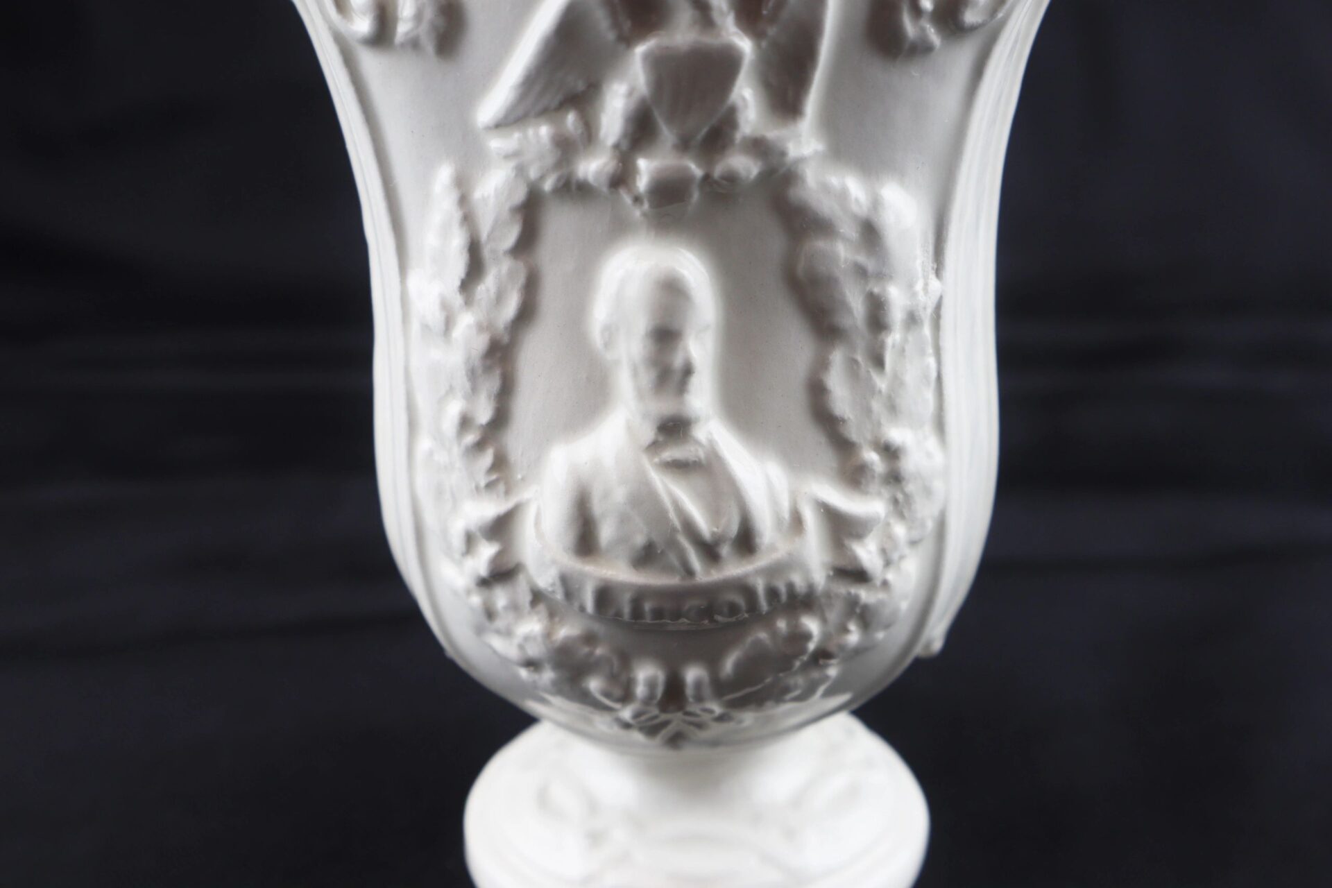 A close-up of the Civil War Vintage Abraham Lincoln Stoneware Vase, featuring a raised, detailed portrait of Lincoln surrounded by ornate decorative elements.
