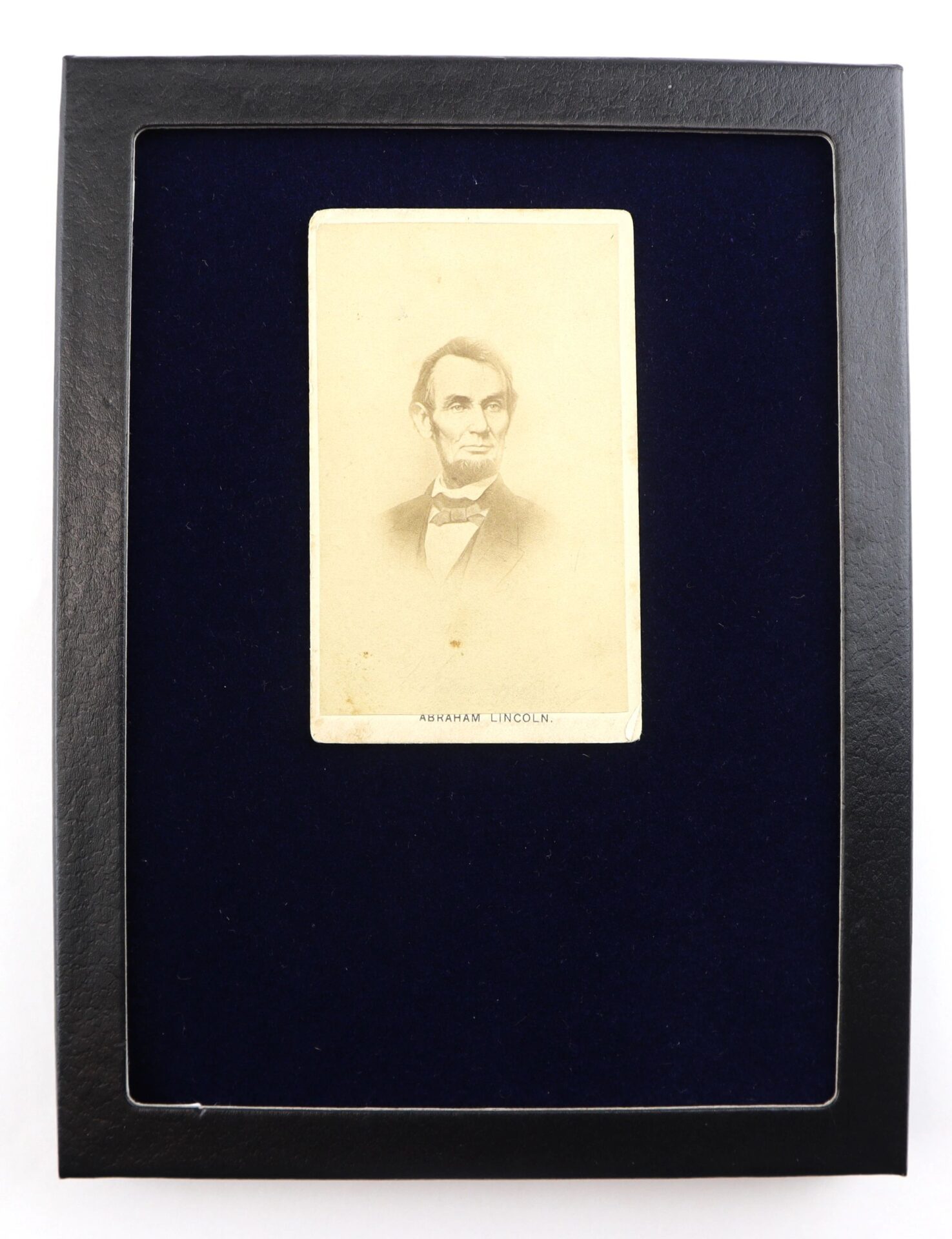 A sepia-toned CDV of Abraham Lincoln, labeled and displayed in a black frame against a dark blue background.