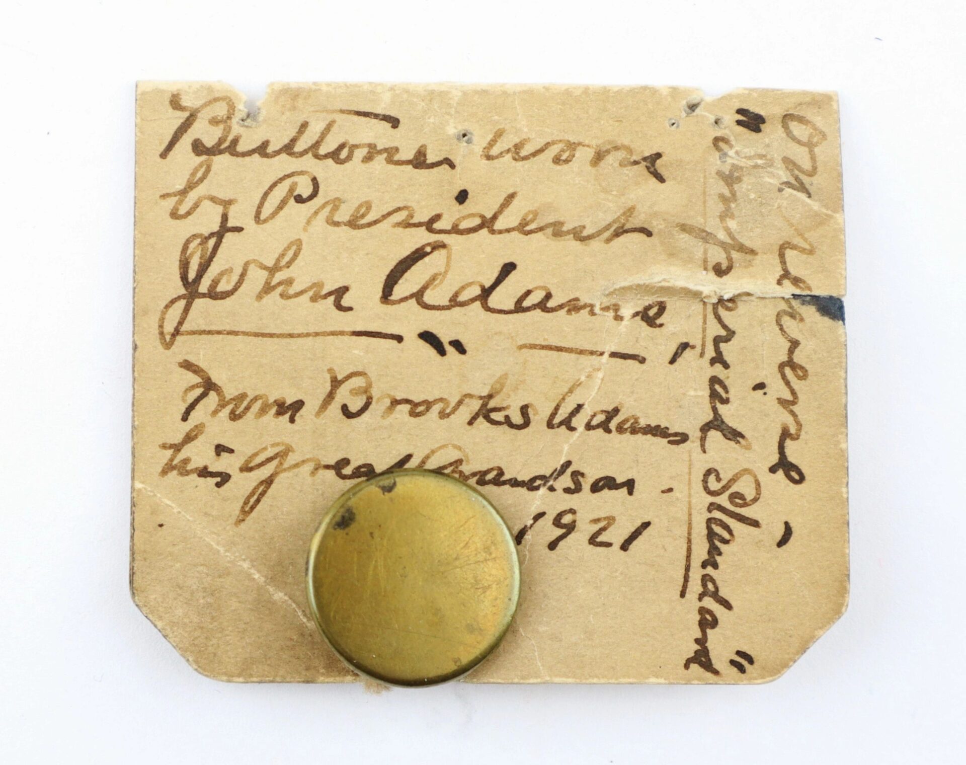 A small brass Button Worn by President John Adams is pinned to a handwritten note from Brooks Adams, signed and dated 1921.