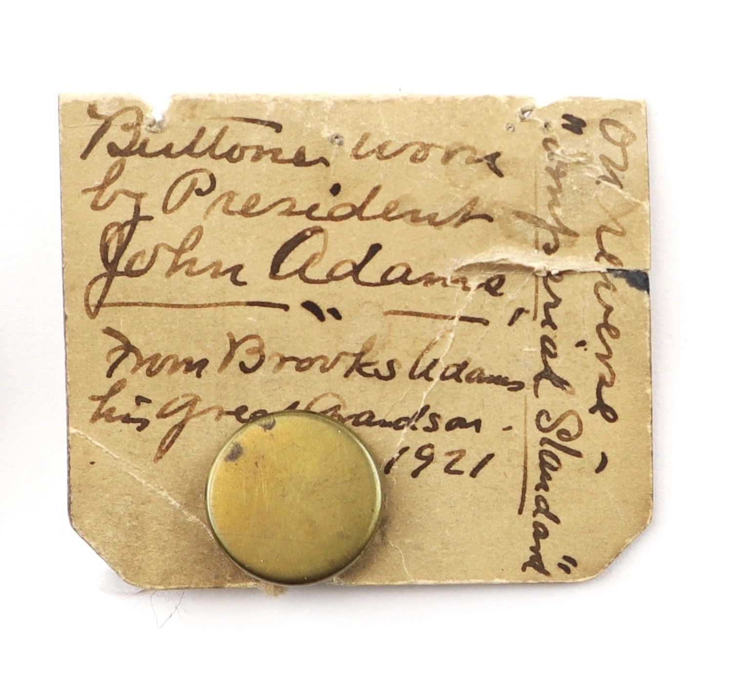 A handwritten paper label with a round brass button, labeled “Button Worn by President John Adams,” and referencing Brooks Adams, 1921.