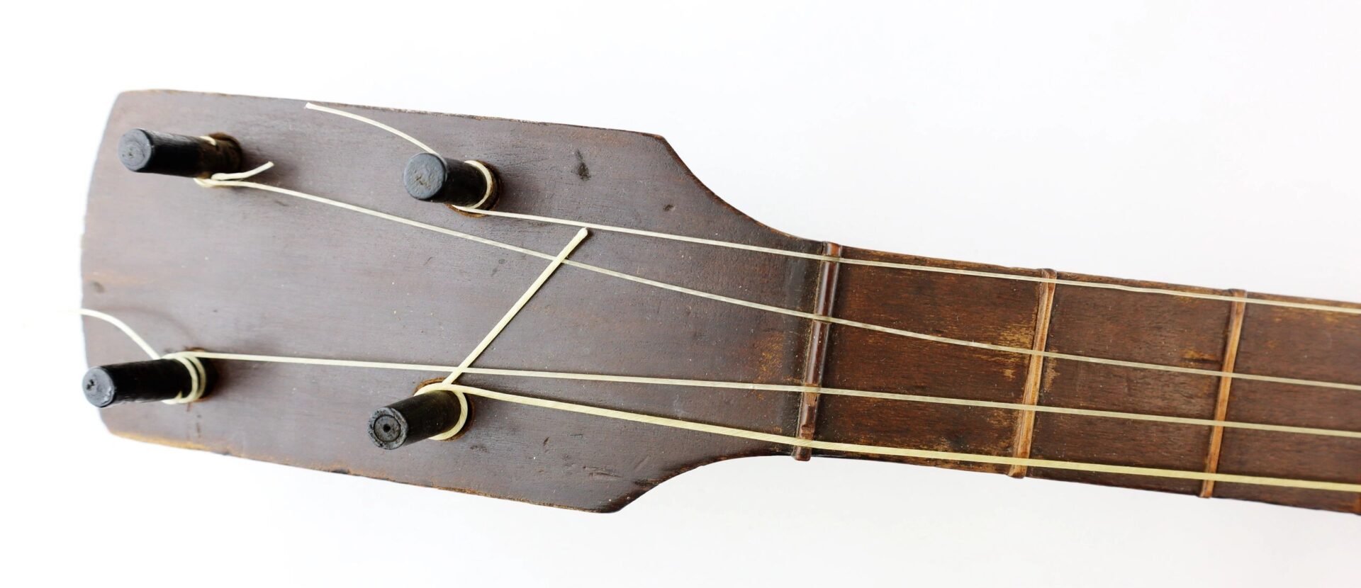 Close-up of a worn Civil War Era Banjo headstock with three tuning pegs and strings, photographed against a white background.