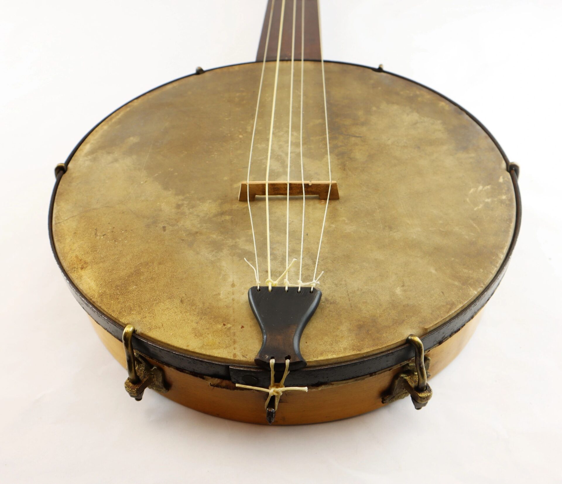 Close-up view of a Civil War Era Banjo, SOLD, highlighting its round worn drumhead, strings, bridge, and wooden rim against a white background.