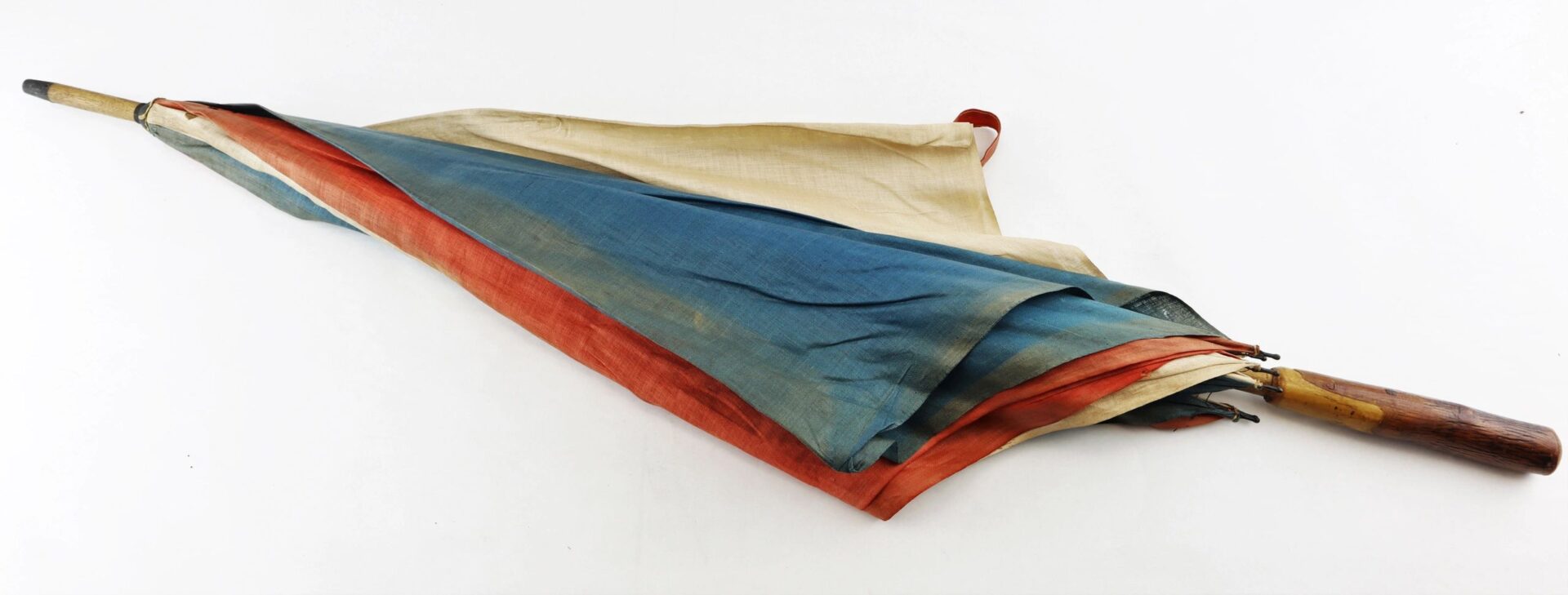 The Patriotic Parasol, a closed umbrella with a wooden handle and multicolored blue, red, and beige fabric, rests on a white background.