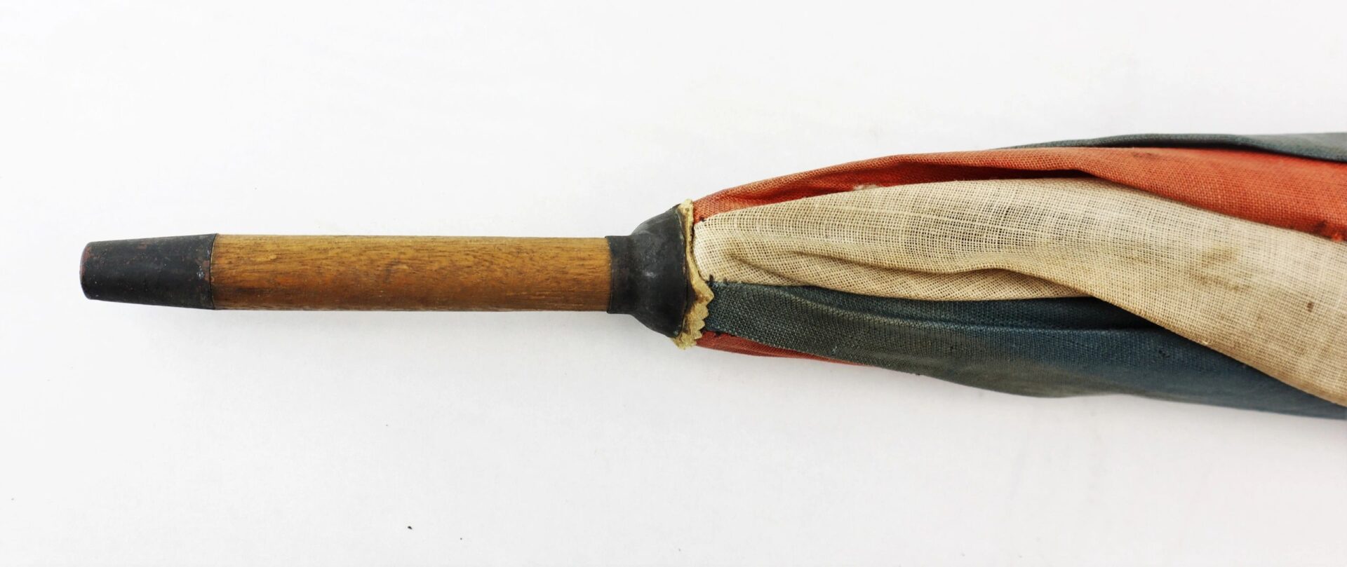Close-up of the tip of a closed Patriotic Parasol, featuring a wooden handle and faded, multicolored fabric.