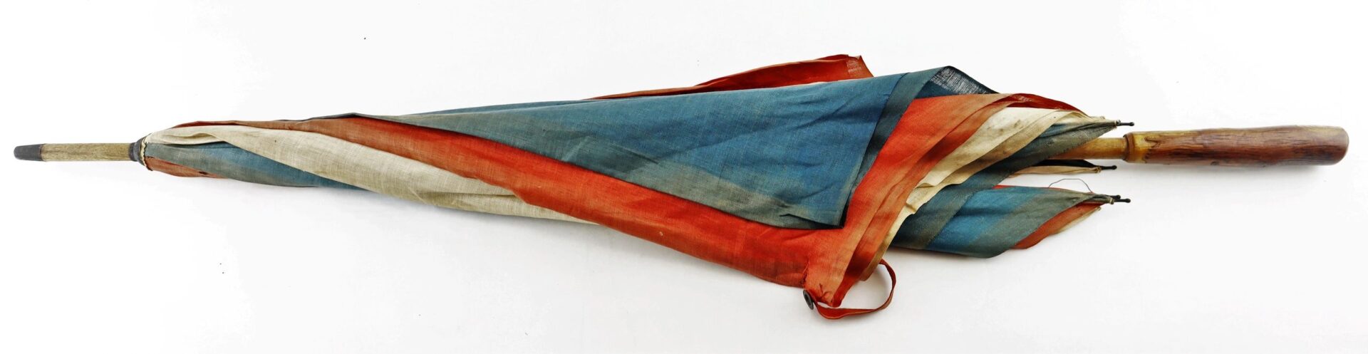 The Patriotic Parasol is a closed vintage umbrella featuring red, blue, and white faded fabric with a wooden handle, displayed against a plain white background.