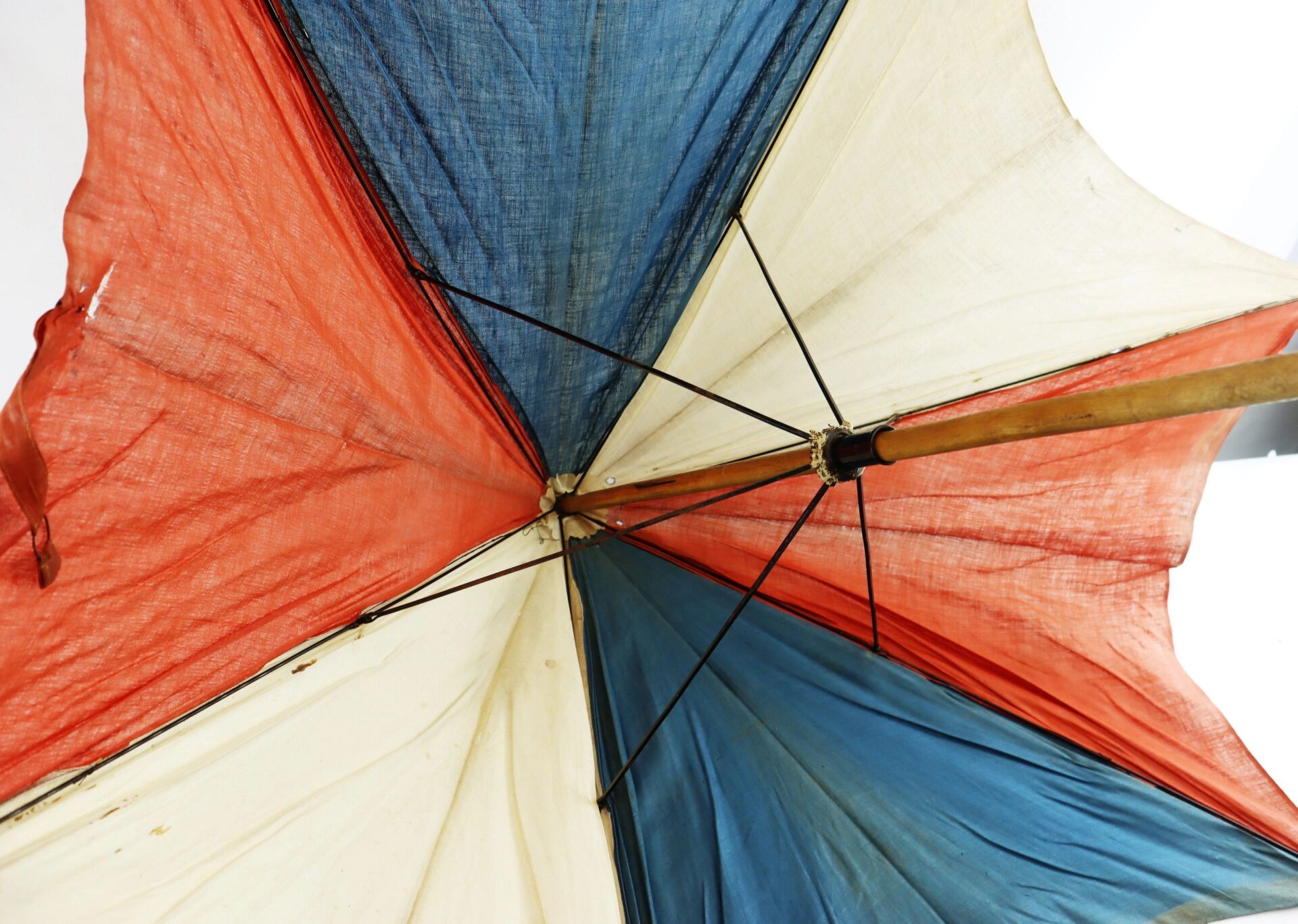 Close-up of the underside of the Patriotic Parasol, featuring red, white, and blue panels with a wooden pole, showing signs of age and wear.