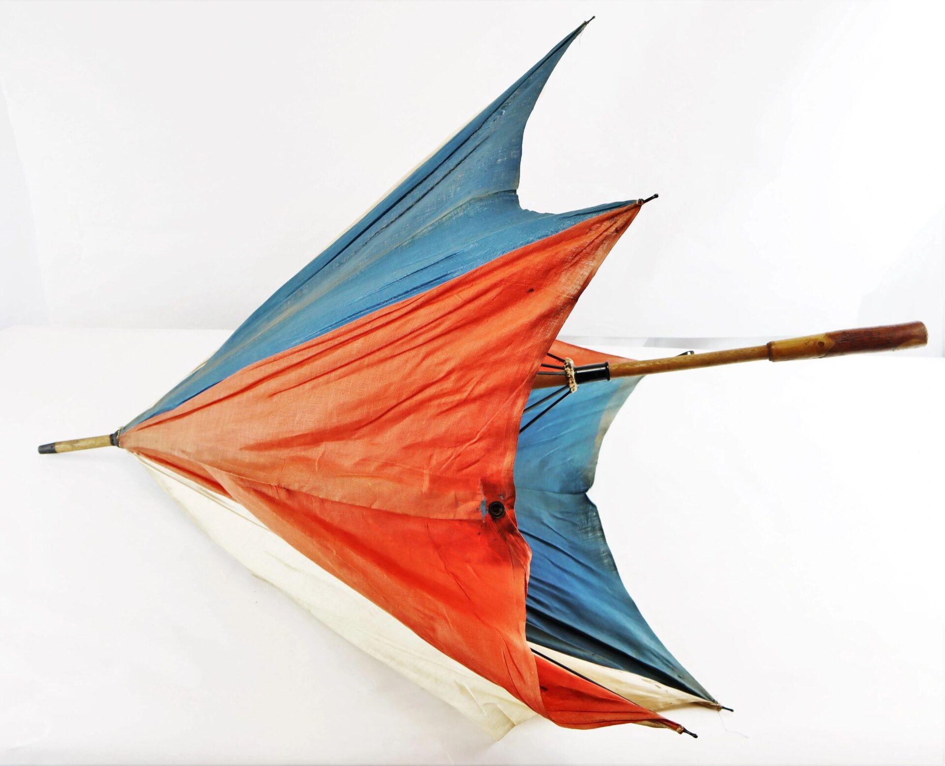 A Patriotic Parasol—red, white, and blue with a wooden handle—is turned inside out by strong wind against a plain white background.